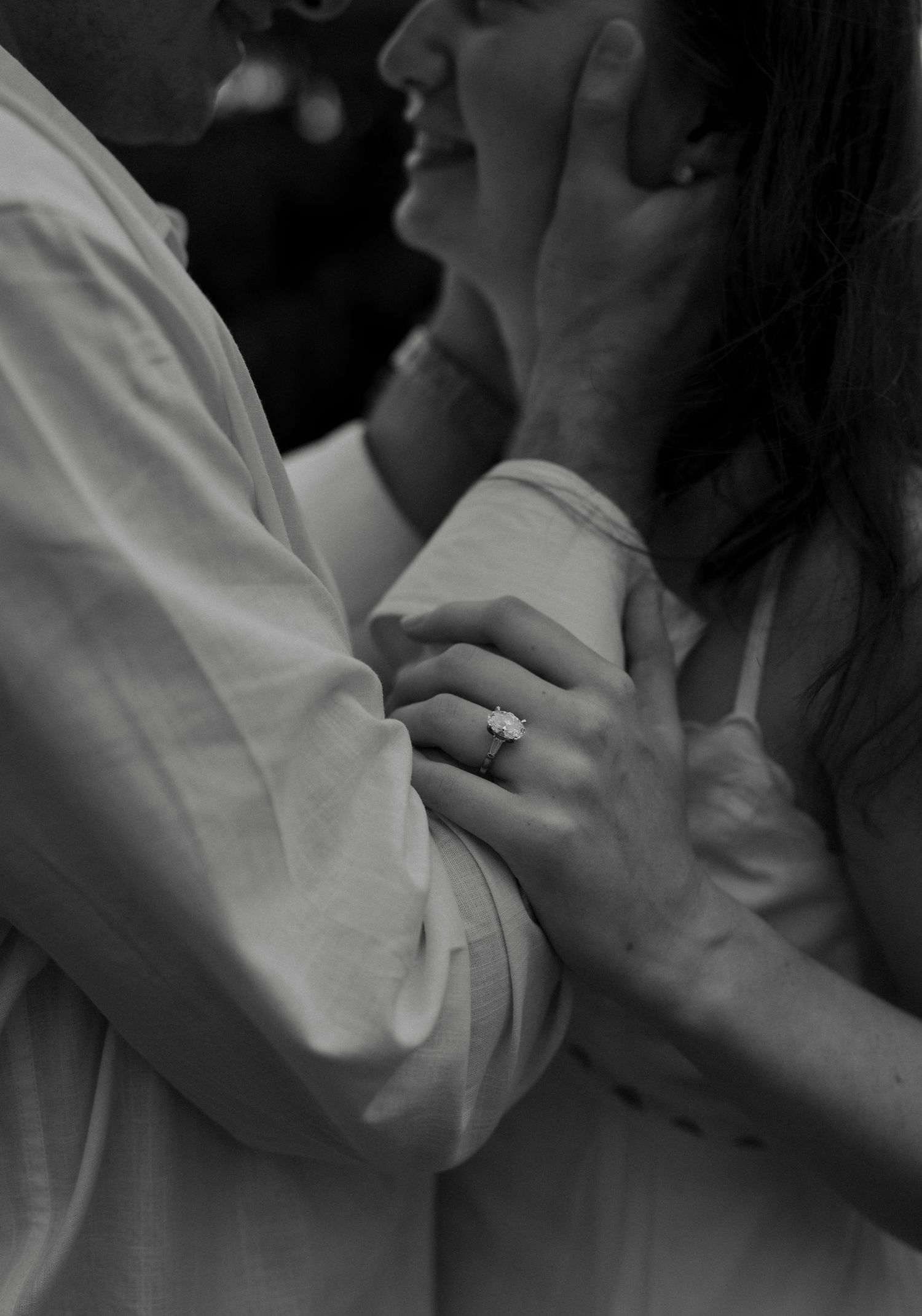 Black and white close-up of couple embracing, showcasing an elegant engagement ring on her hand.