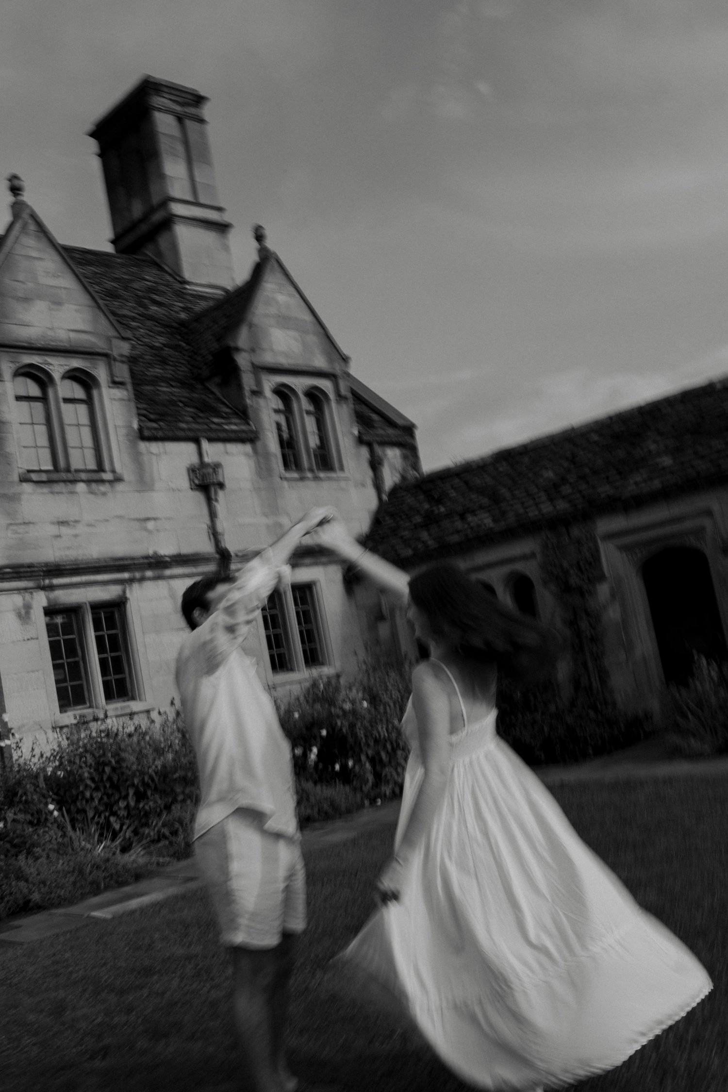 Black and white photo of a couple dancing gracefully in front of a historic stone manor house.