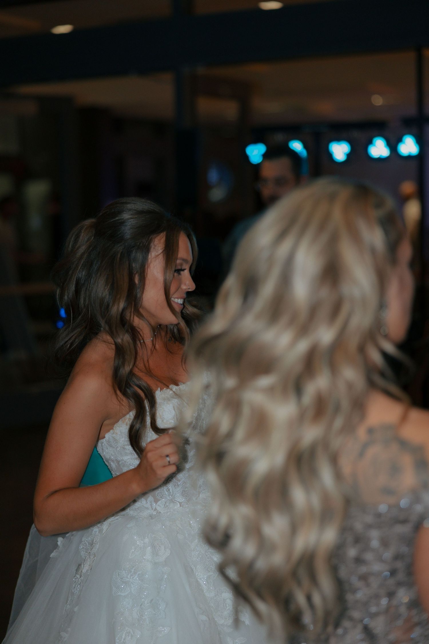 Bride in lace gown laughs joyfully with guests during wedding reception dance floor celebration.