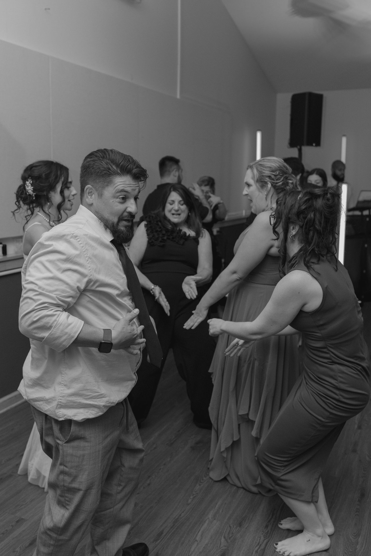 Wedding guests dancing joyfully on the dance floor in black and white photo at a reception celebration.