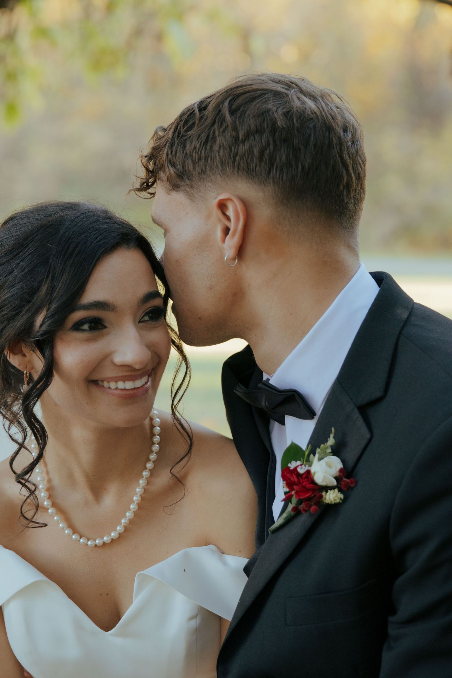 Bride smiling as groom kisses her cheek during outdoor wedding portrait session.