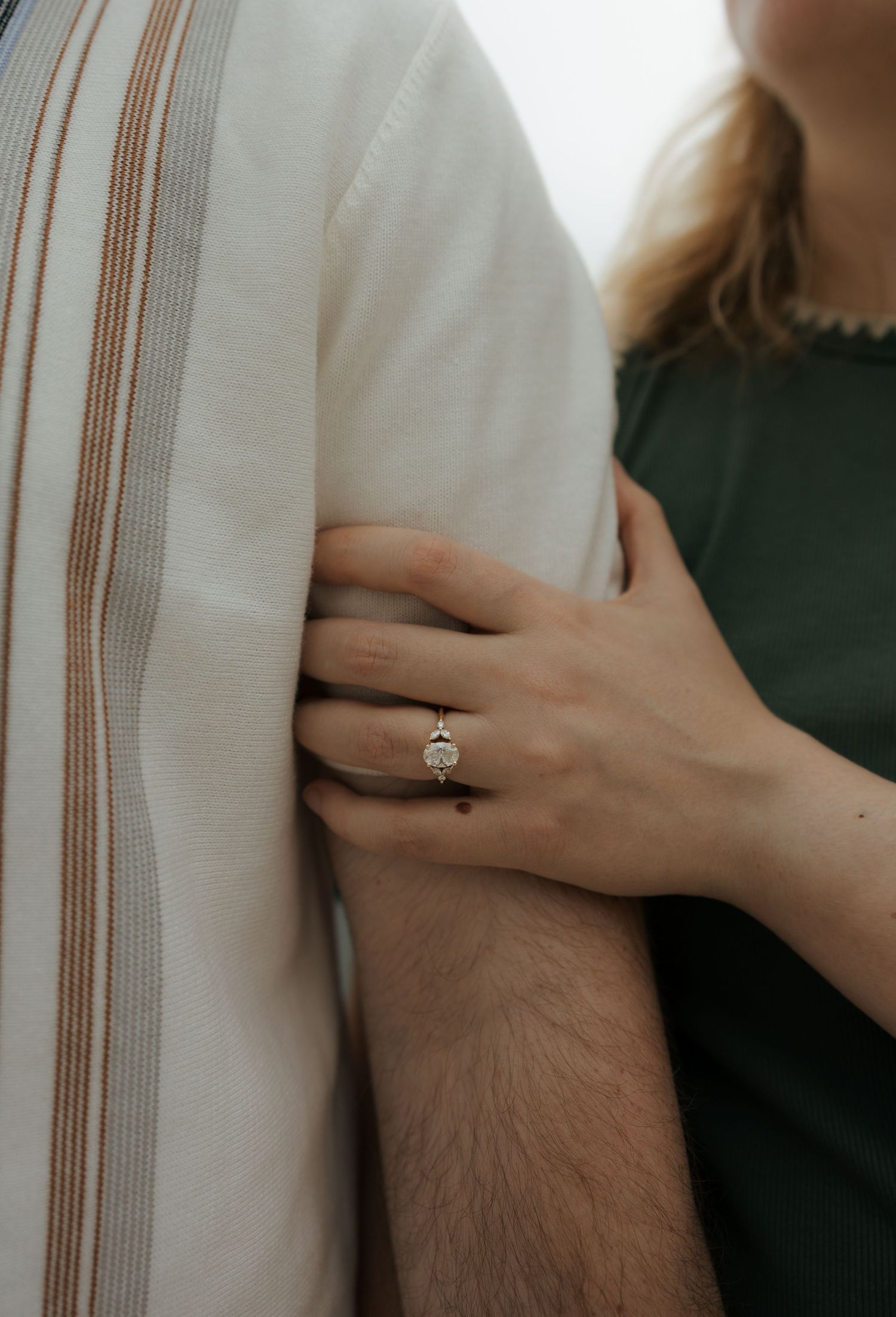Close-up of a woman's hand gripping a man's arm, showcasing a elegant solitaire diamond engagement ring.