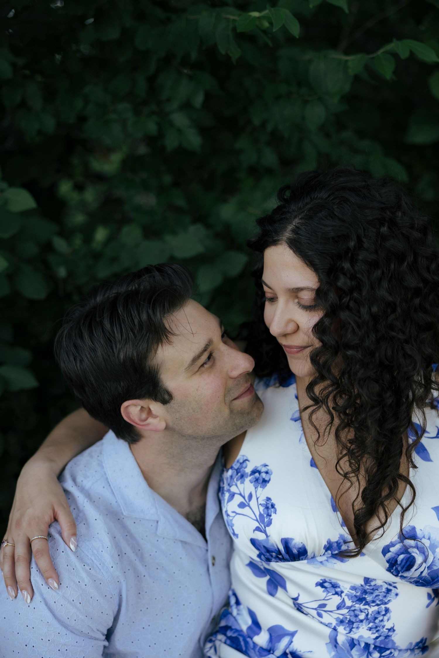 A couple gazes lovingly at each other outdoors surrounded by lush green foliage.