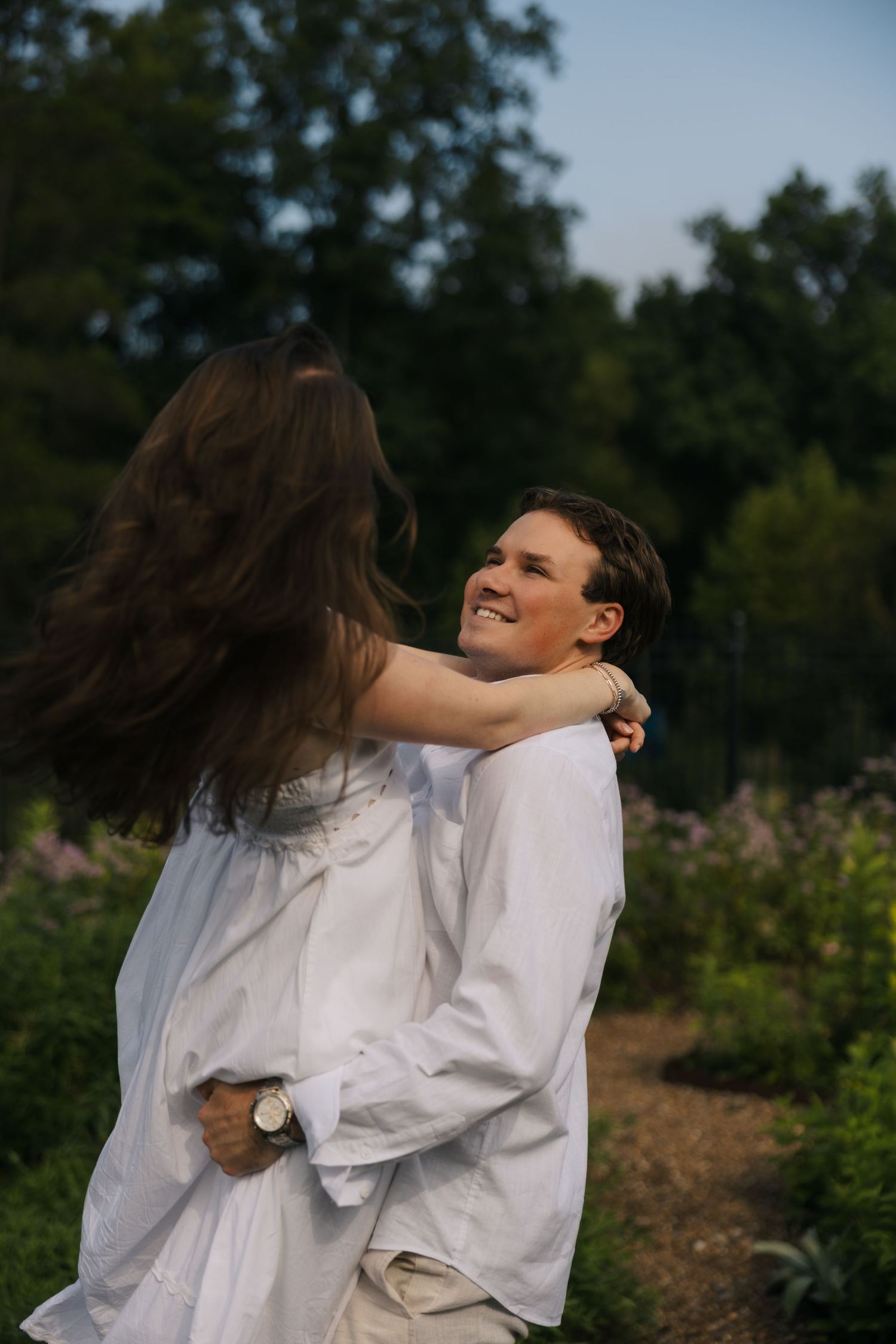 Joyful couple embracing and smiling in a lush garden at golden hour dusk.