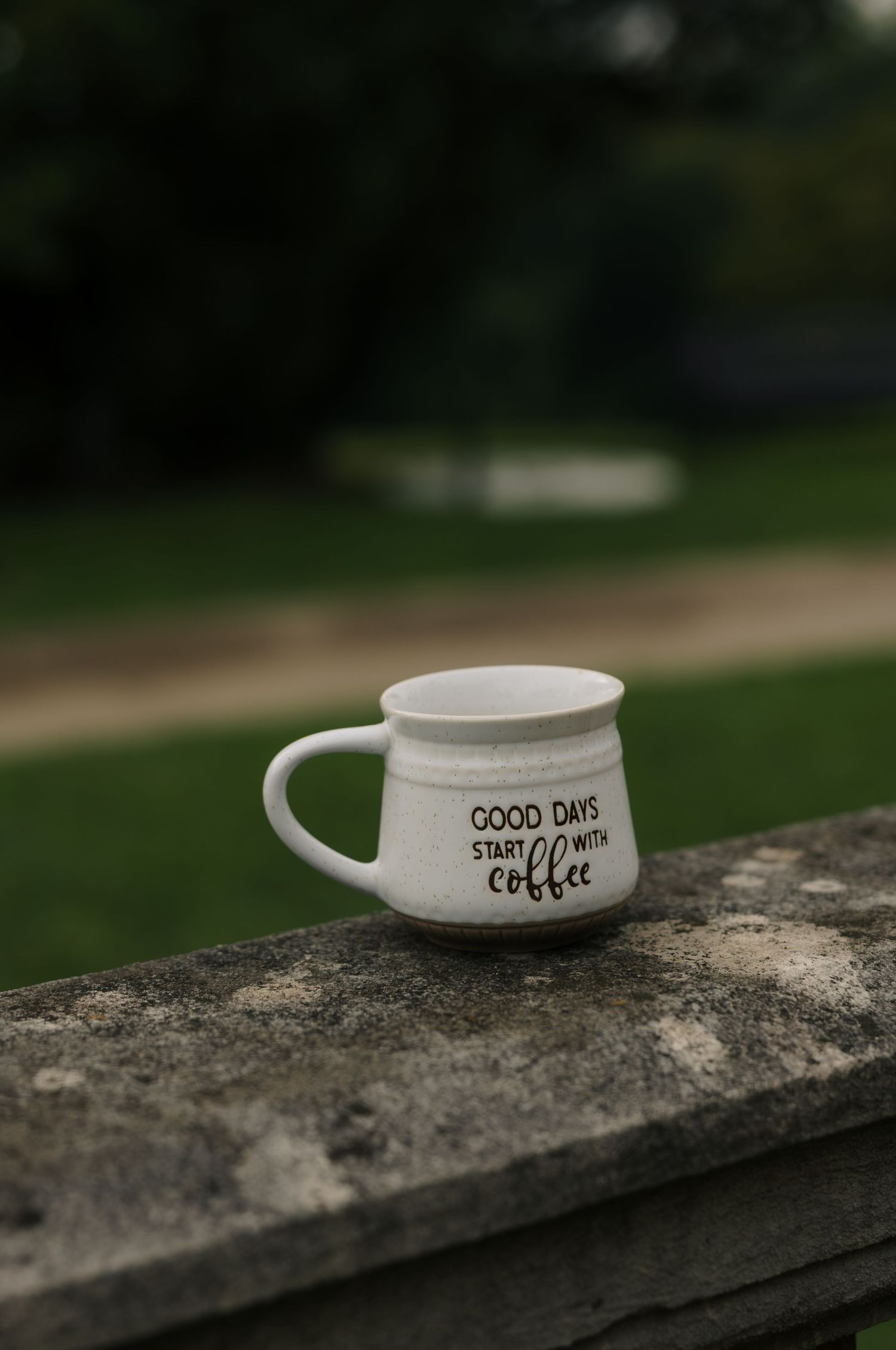 White ceramic mug reading Good Days Start With Coffee on stone ledge.