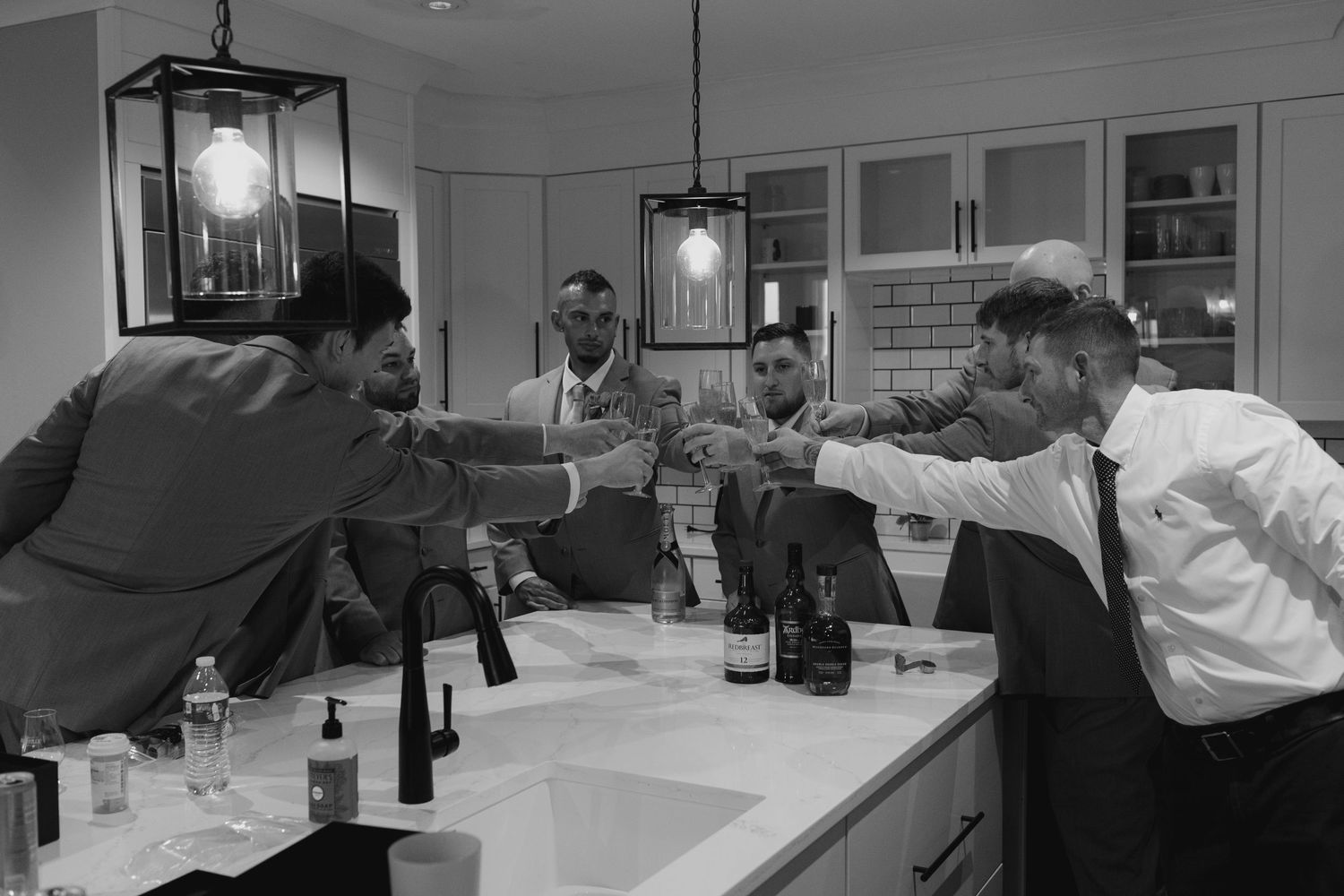 Groomsmen celebrating with a toast over a bathroom counter in black and white wedding photo.