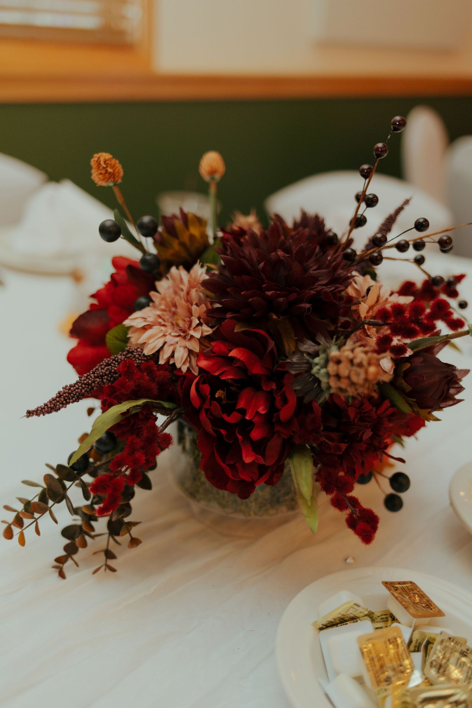 Elegant fall wedding centerpiece with burgundy dahlias and berries.