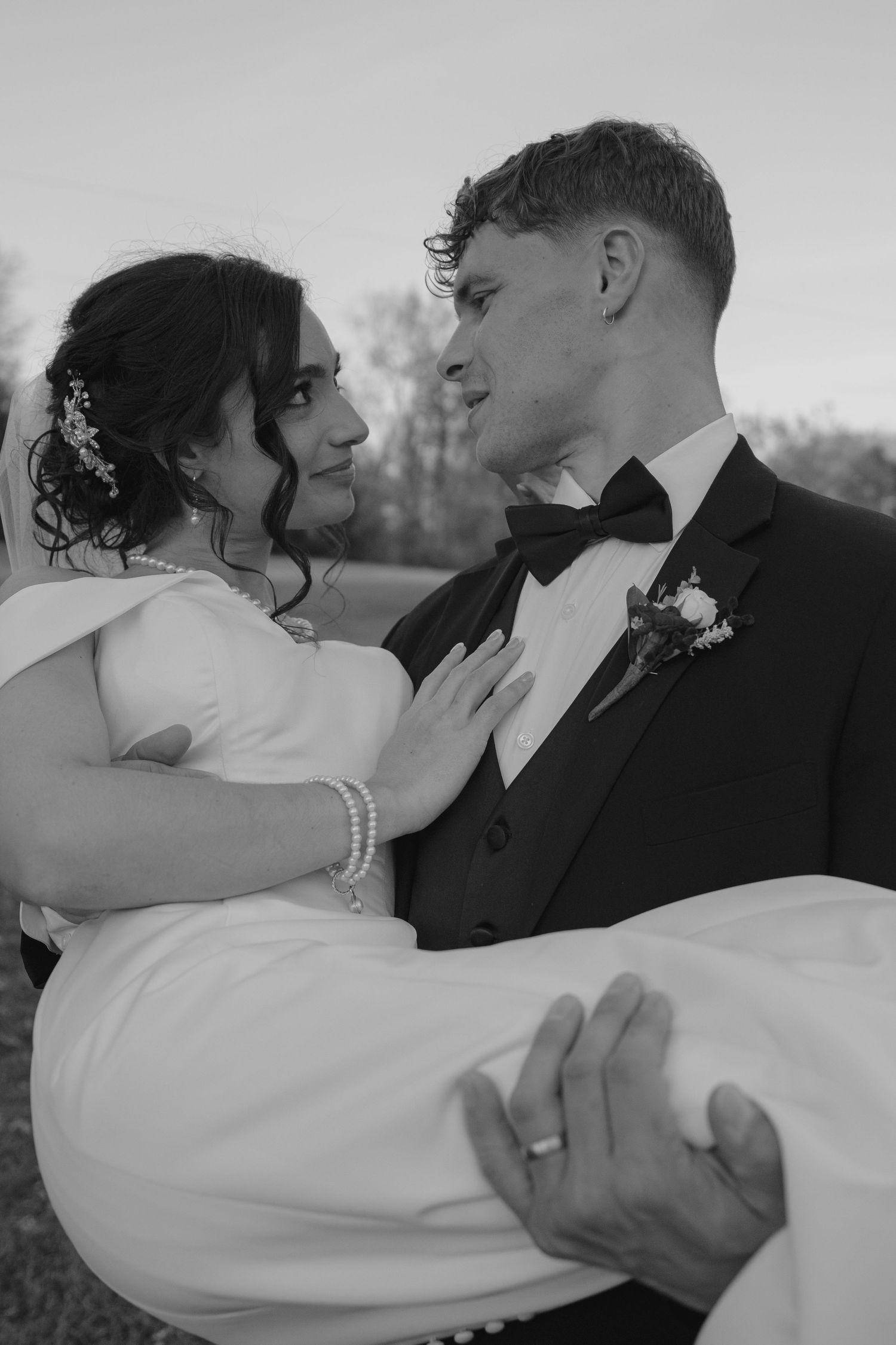 Black and white photo of groom carrying bride in his arms, both gazing at each other tenderly.