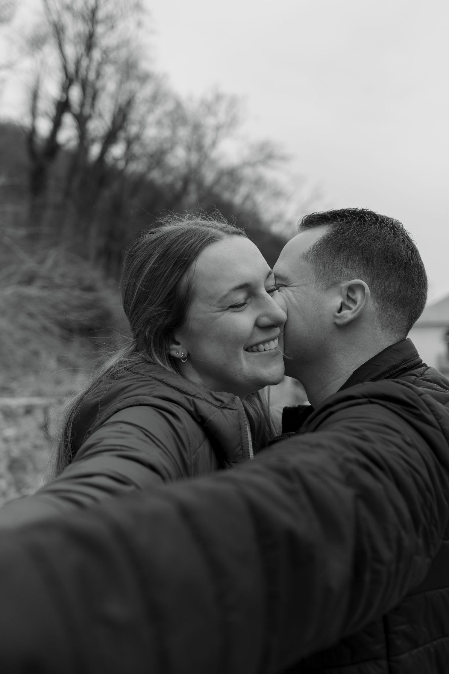 A romantic black and white photo series showing a couple embracing and sharing tender moments outdoors.