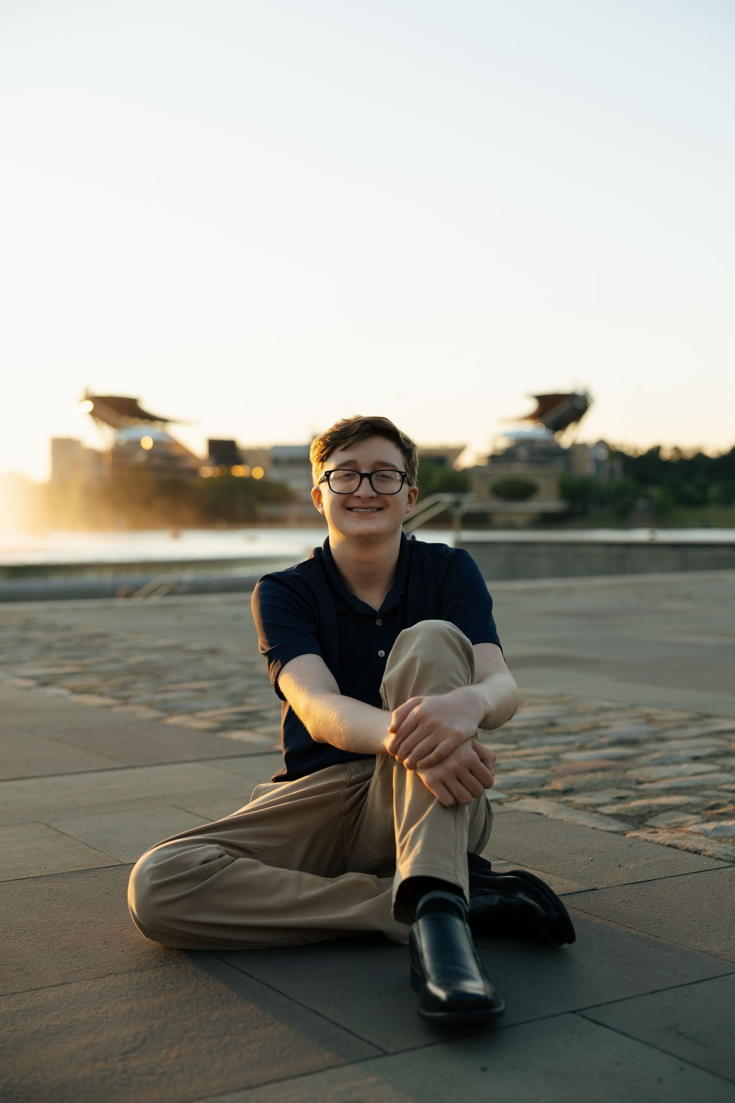 Teen boy sitting cross-legged on plaza at golden hour sunset.