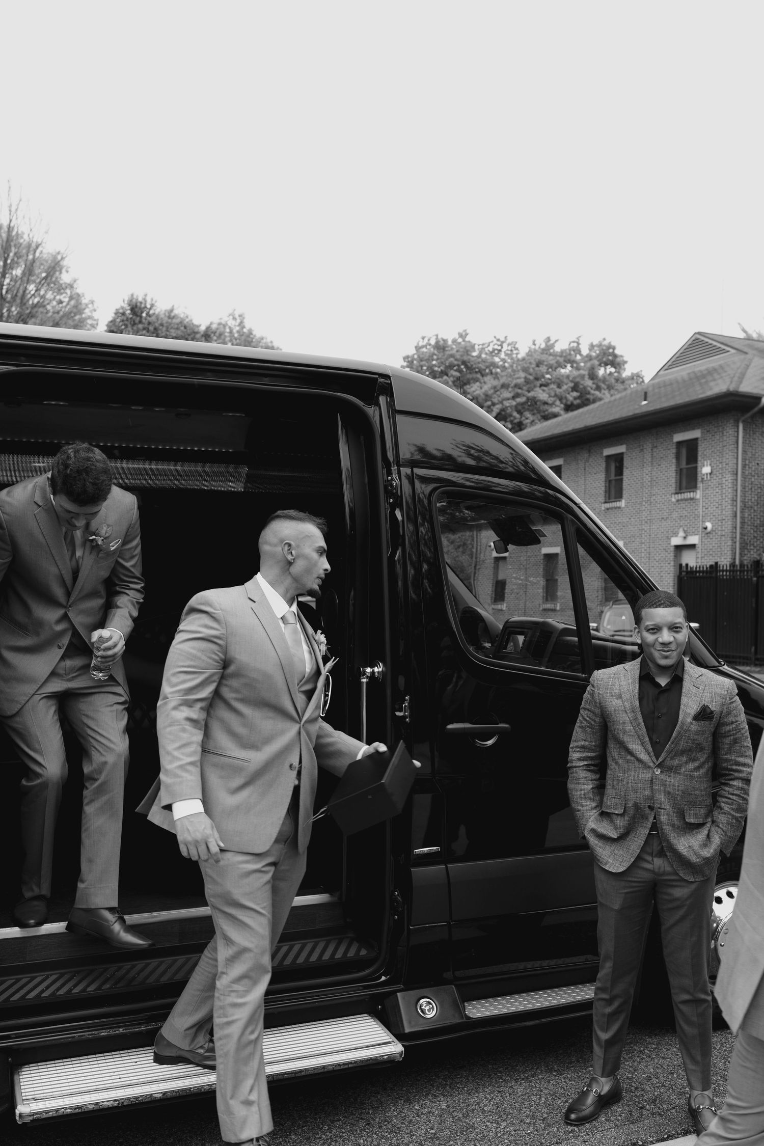 Groomsmen in suits stepping out of a black luxury van on a wedding day.