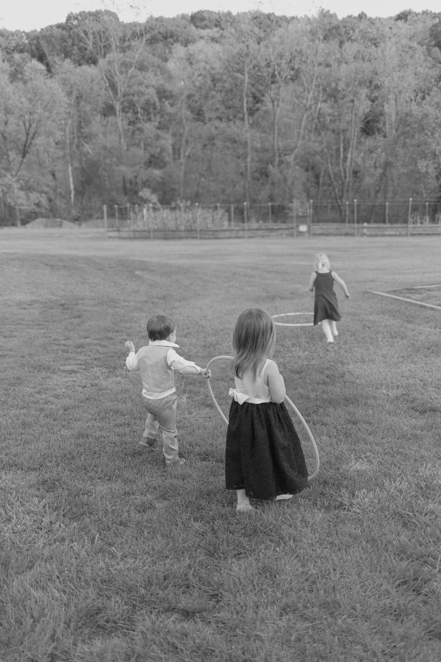Three children play with hula hoops on grassy field at outdoor wedding reception.