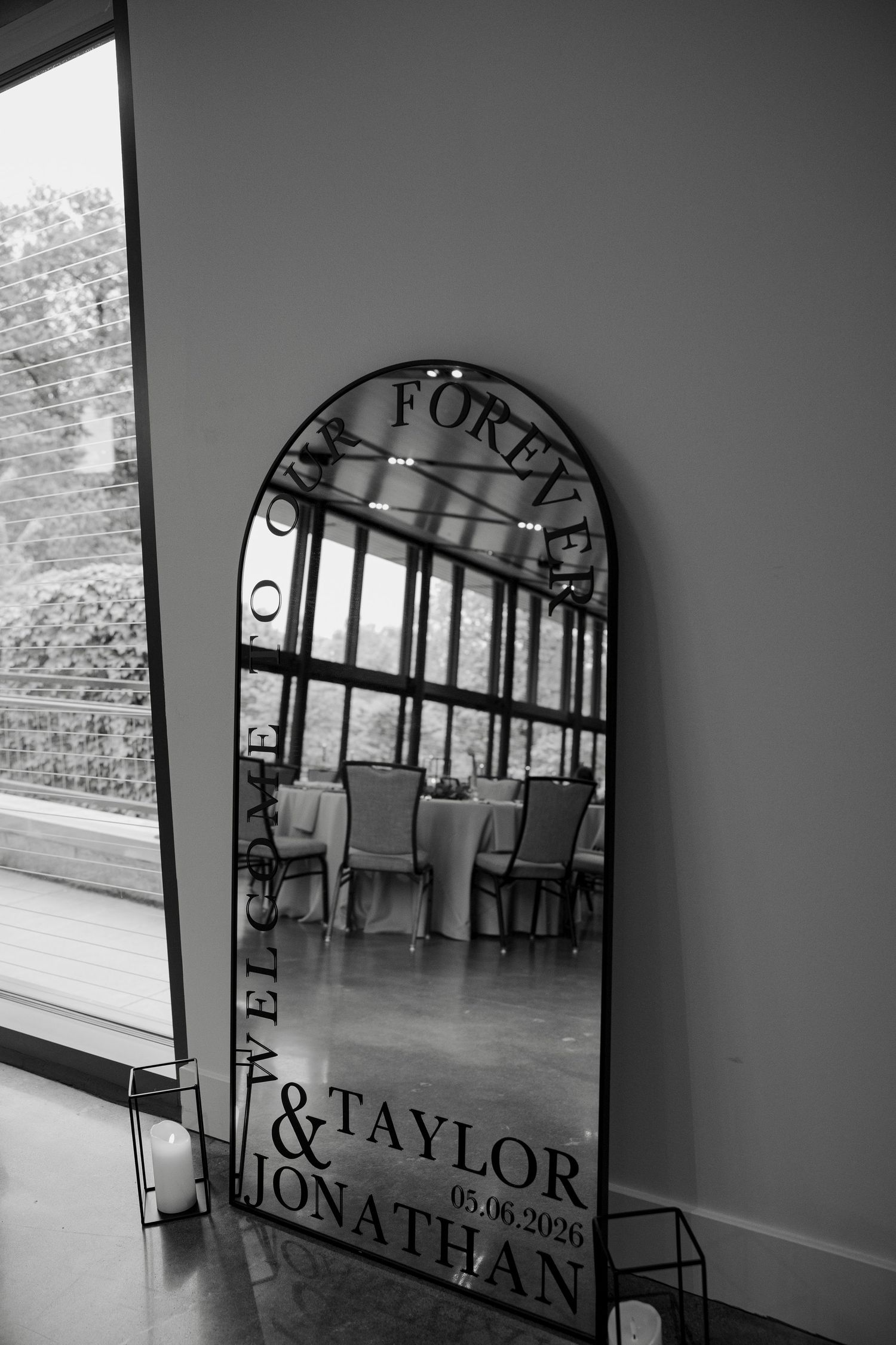 Elegant arched wedding mirror with Taylor & Jonathan Forever text, reflecting decorated reception tables in black and white.
