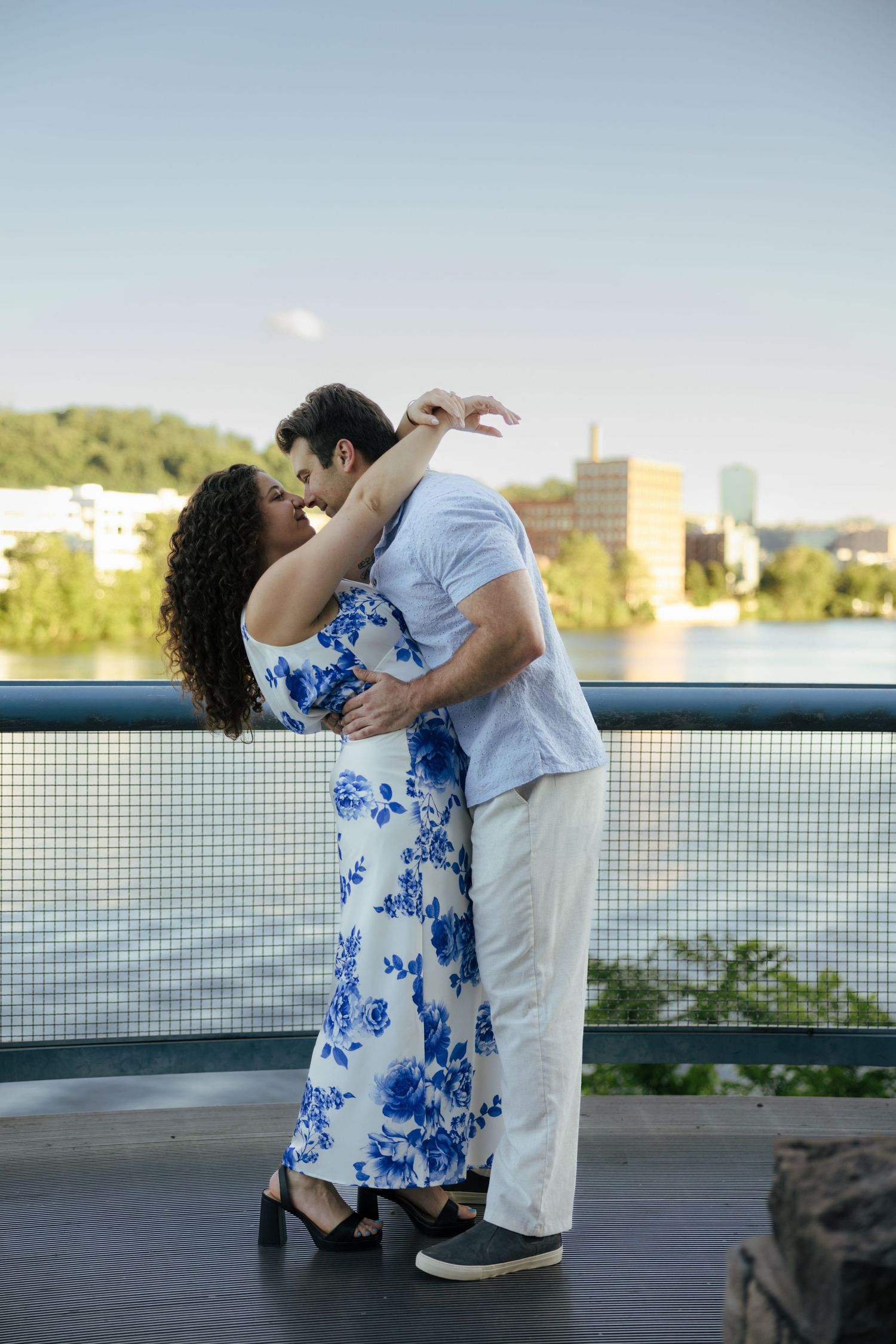 Couple sharing a romantic kiss while dancing on a riverside deck at golden hour.