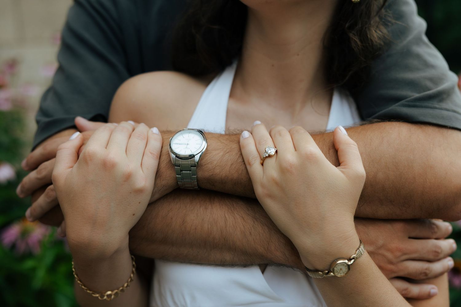Close-up of couple's hands embracing, showcasing an engagement ring, gold bracelet, and silver watch.