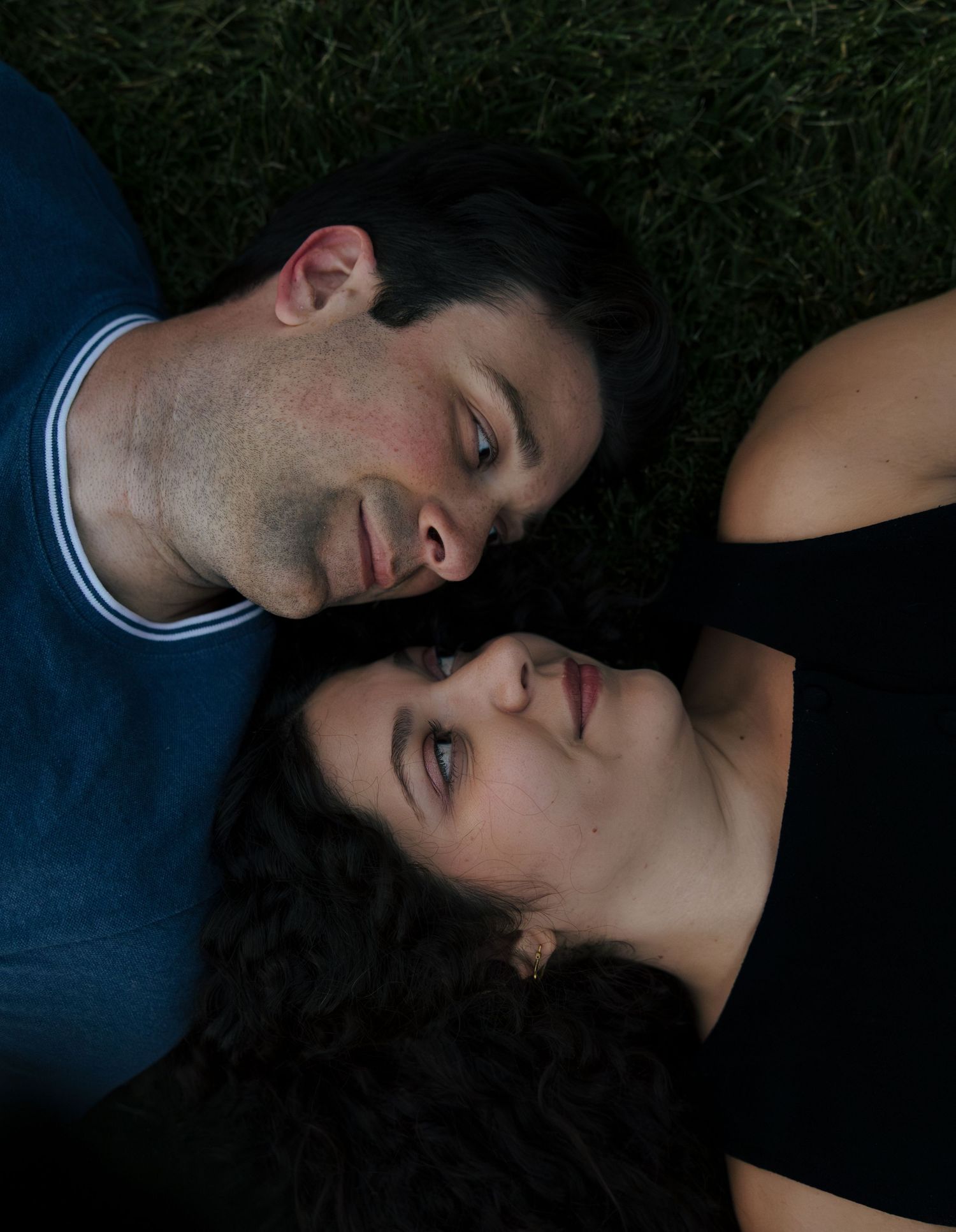 Couple lying on grass gazing at each other in an intimate close-up portrait shot from above.