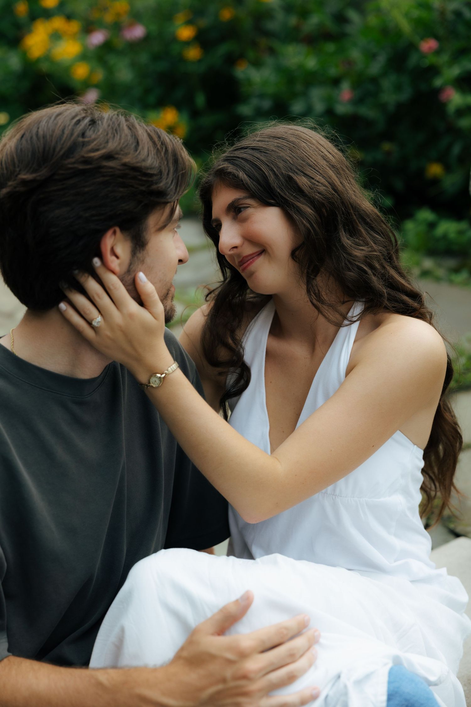 Couple sharing an intimate moment outdoors, woman in white dress tenderly holding mans face.