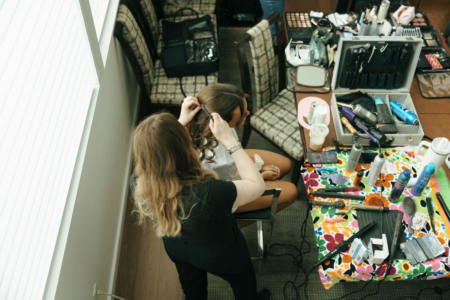 Overhead view of a hair stylist working on a bride surrounded by beauty tools and colorful accessories.