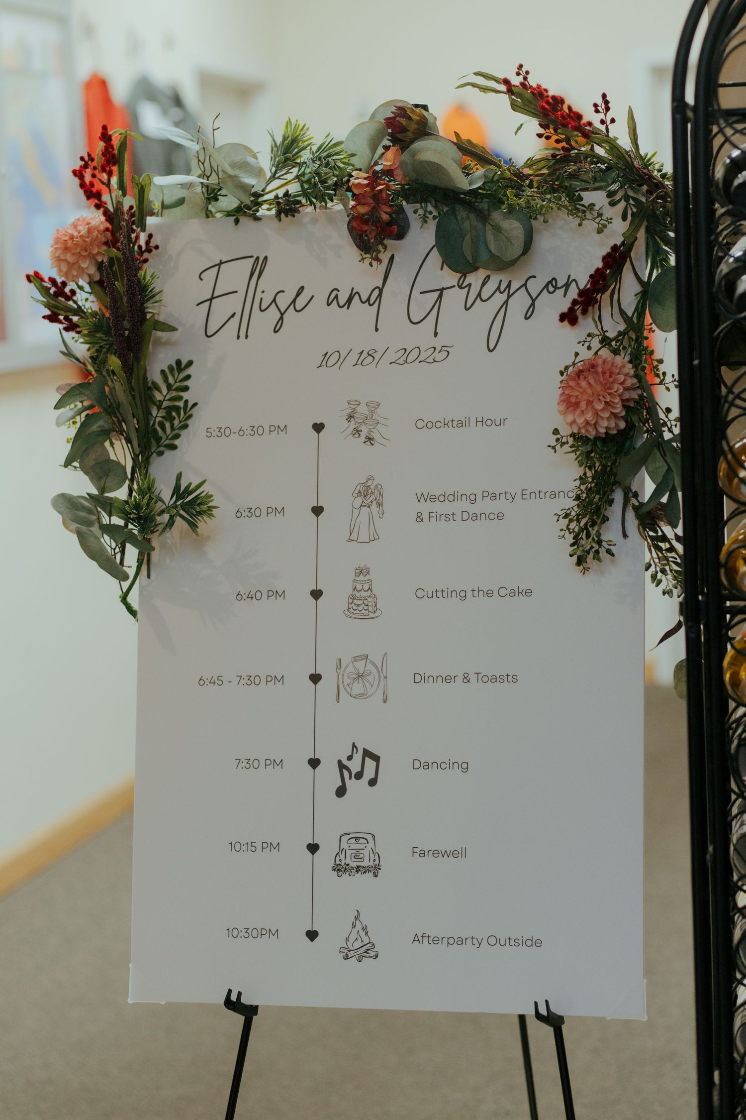 Wedding reception timeline sign for Ellise and Greyson dated 10/18/2023 decorated with floral greenery and berries.