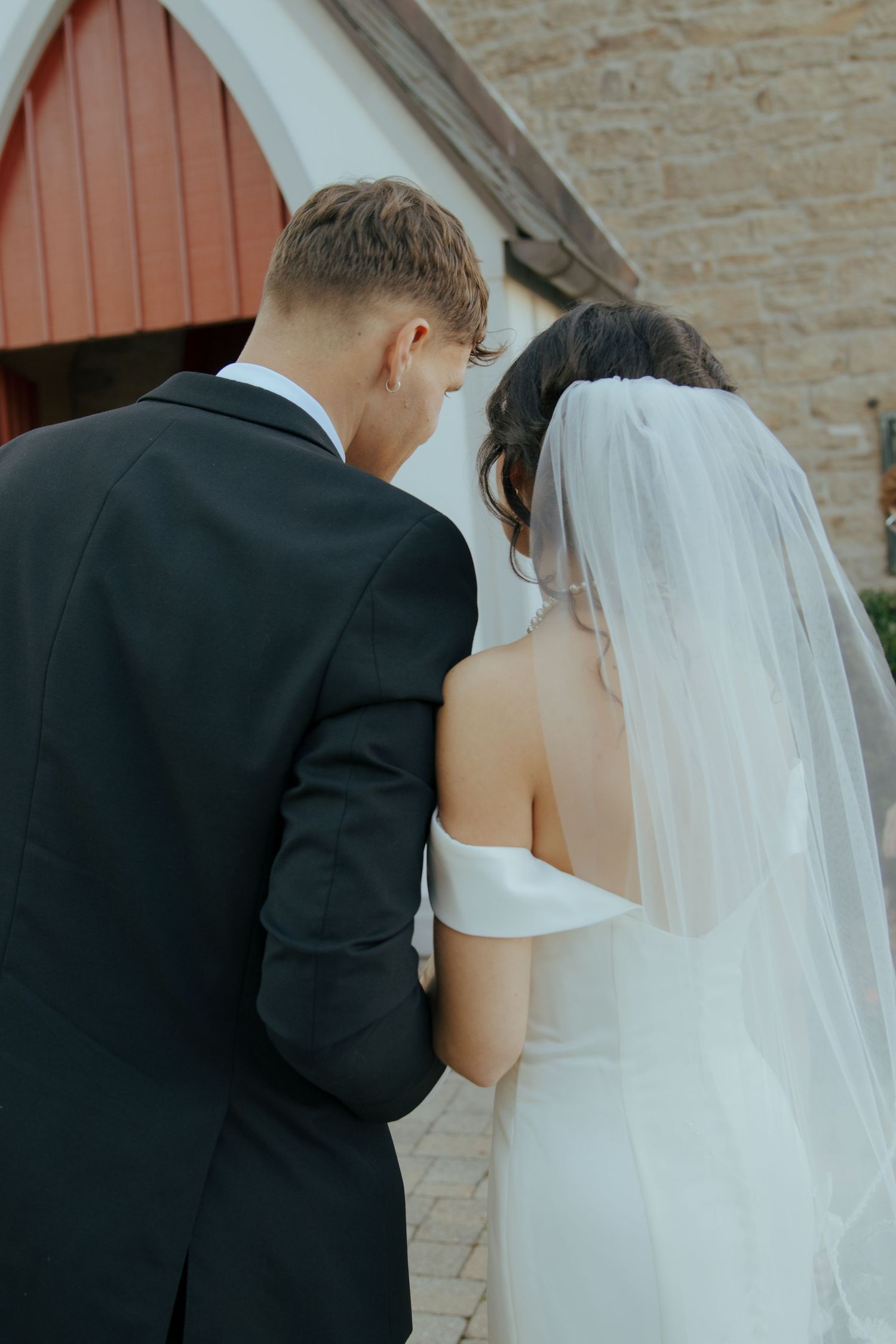 Bride in veil and groom walk arm in arm outside church.