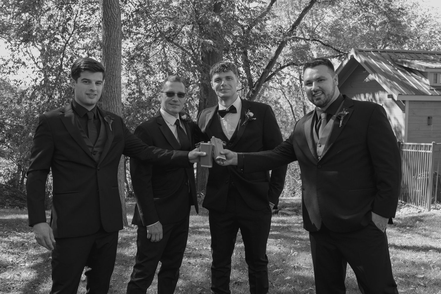 Four men in suits pose together outdoors in a black and white wedding photo.