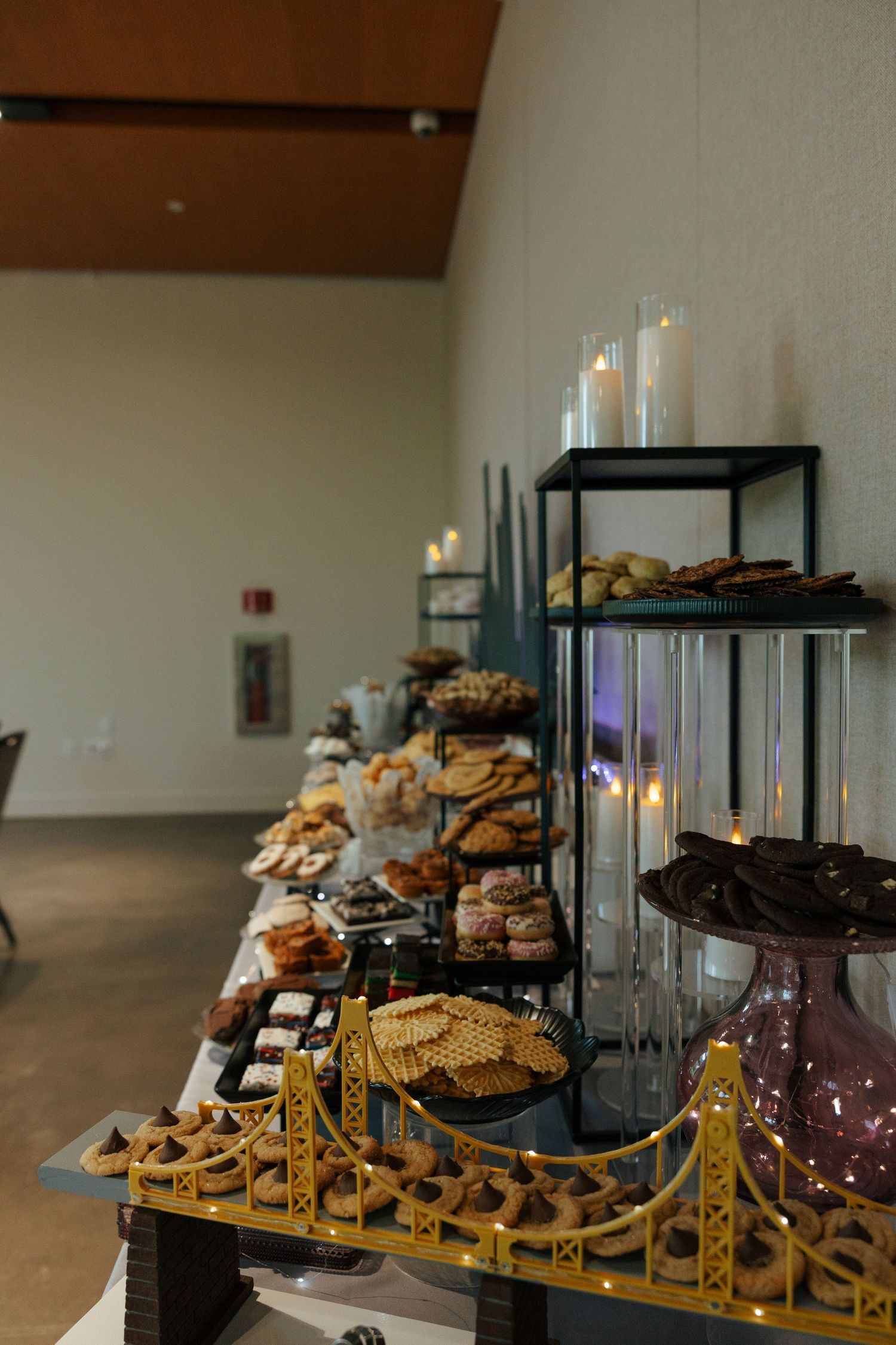 Elegant dessert table display with candles, assorted pastries, and a decorative golden bridge centerpiece at an event.