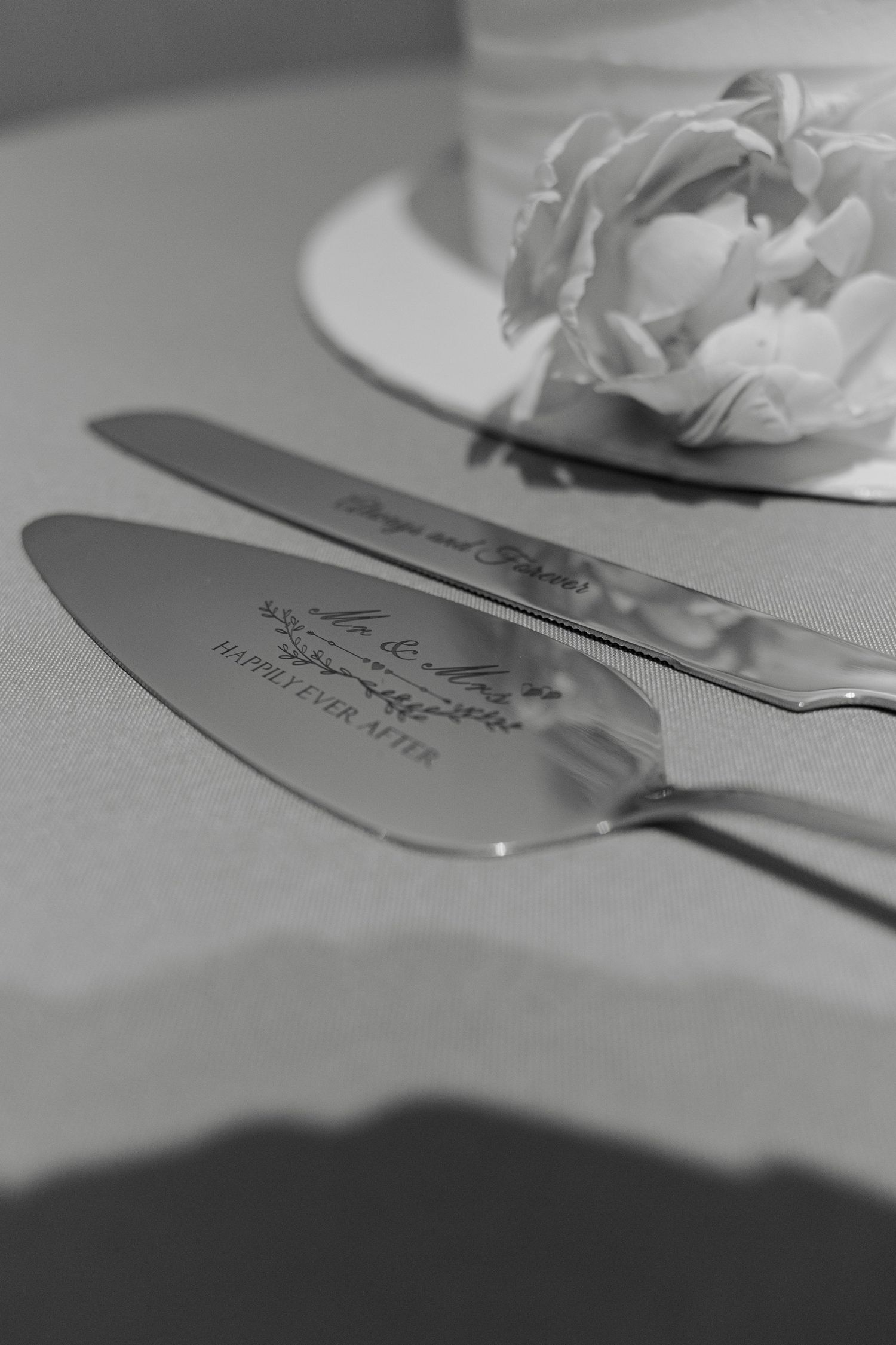 Engraved silver wedding cake knife and server set with Mr. & Mrs. and Happily Ever After inscription on white tablecloth.