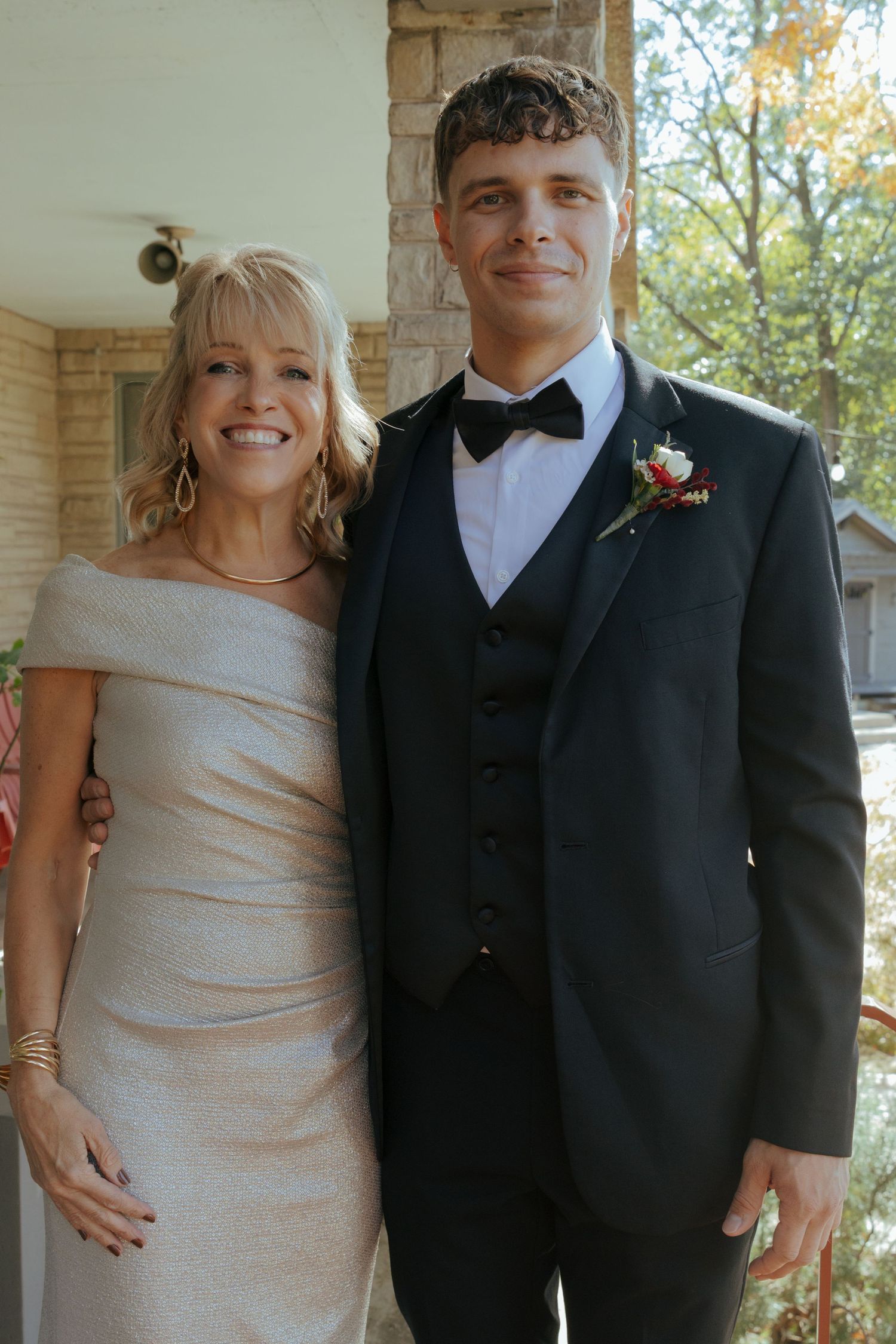 Smiling mother poses with handsome groom in black tuxedo and boutonniere before wedding ceremony.