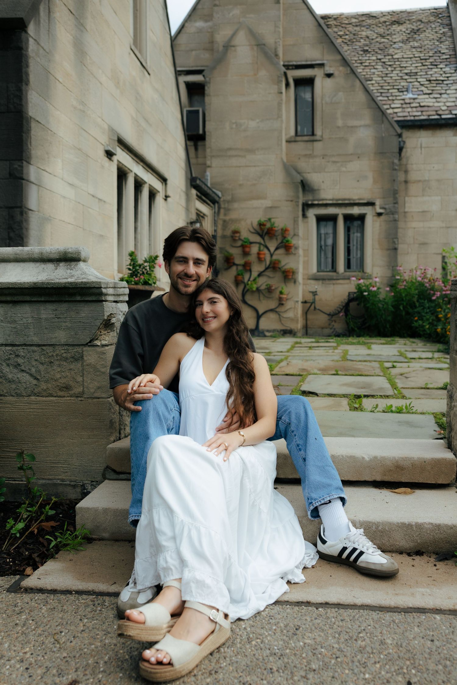 Happy couple sitting together on stone steps outside a charming vintage stone manor house.