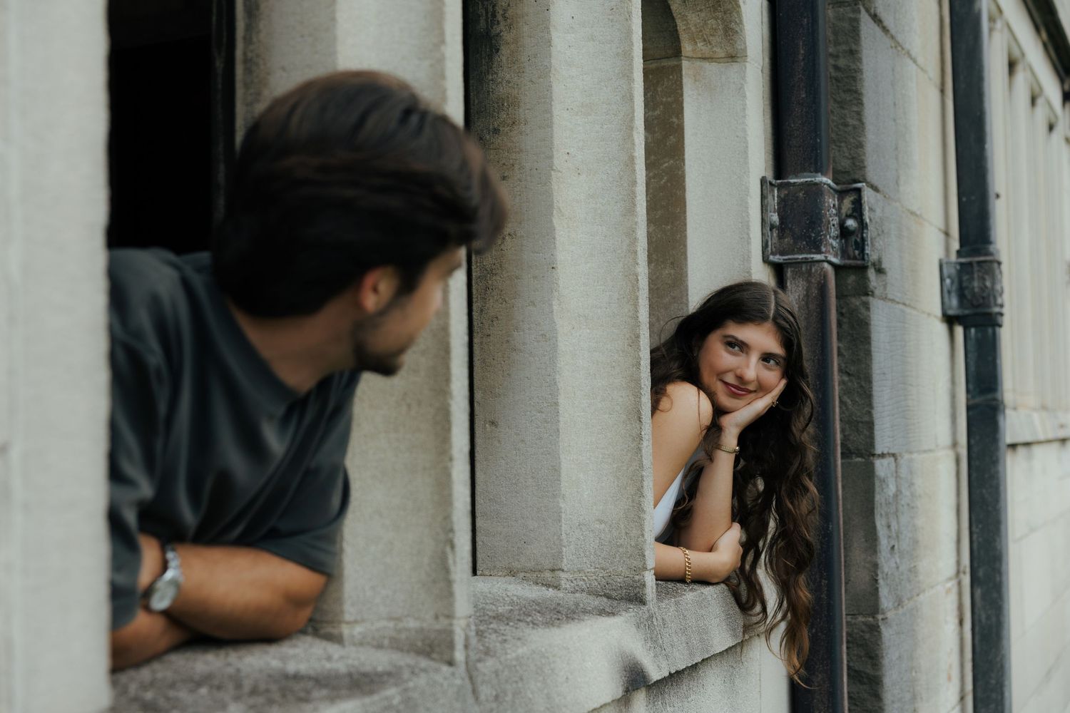 A woman smiles warmly at a man from a stone archway during an outdoor couples portrait session.