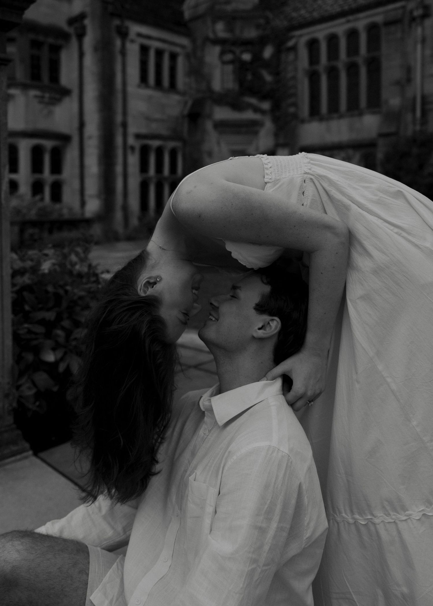 Black and white romantic photo of couple leaning in for a kiss before stone manor.