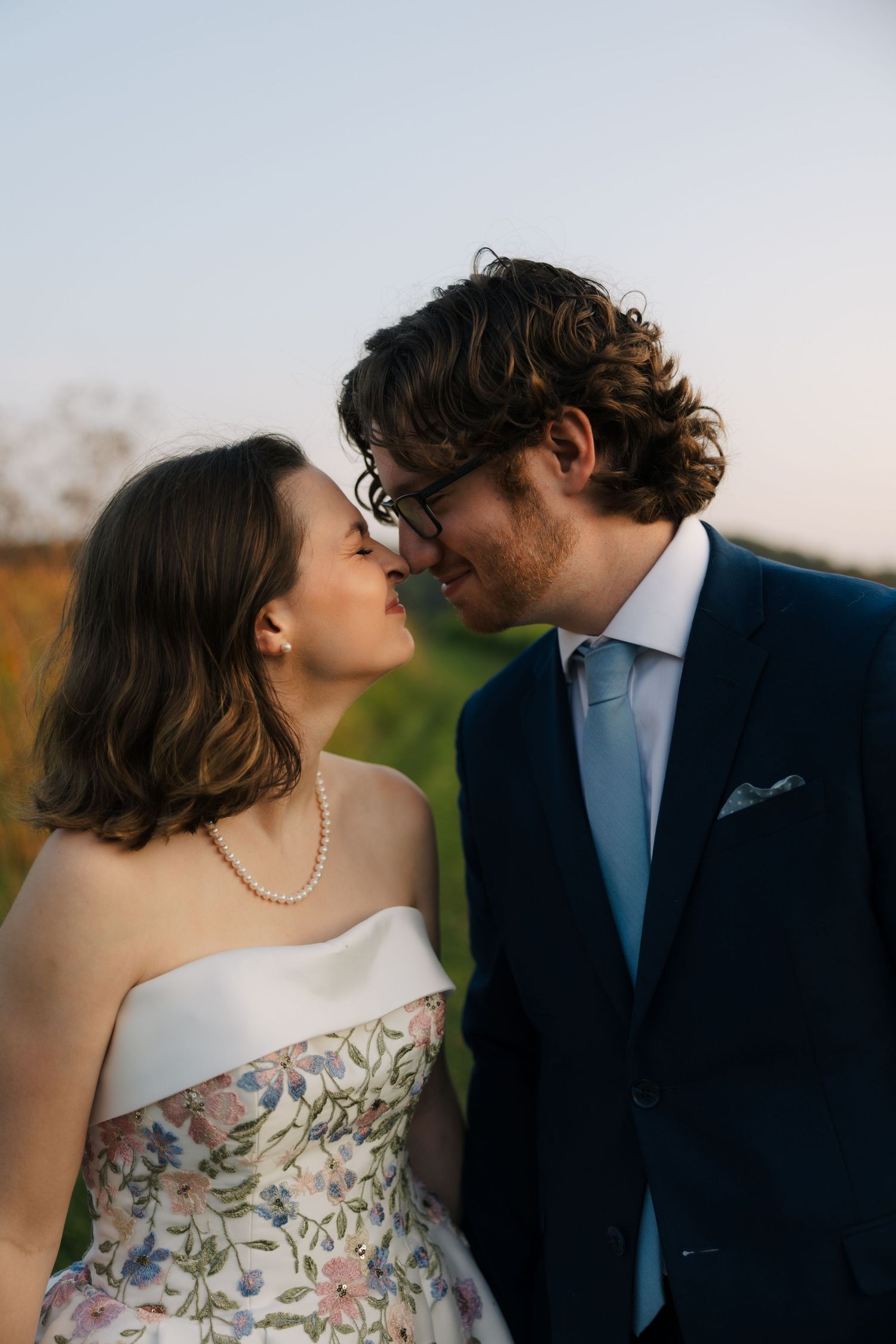Bride and groom sharing an intimate almost-kiss moment outdoors at golden hour, bride wearing floral wedding gown.