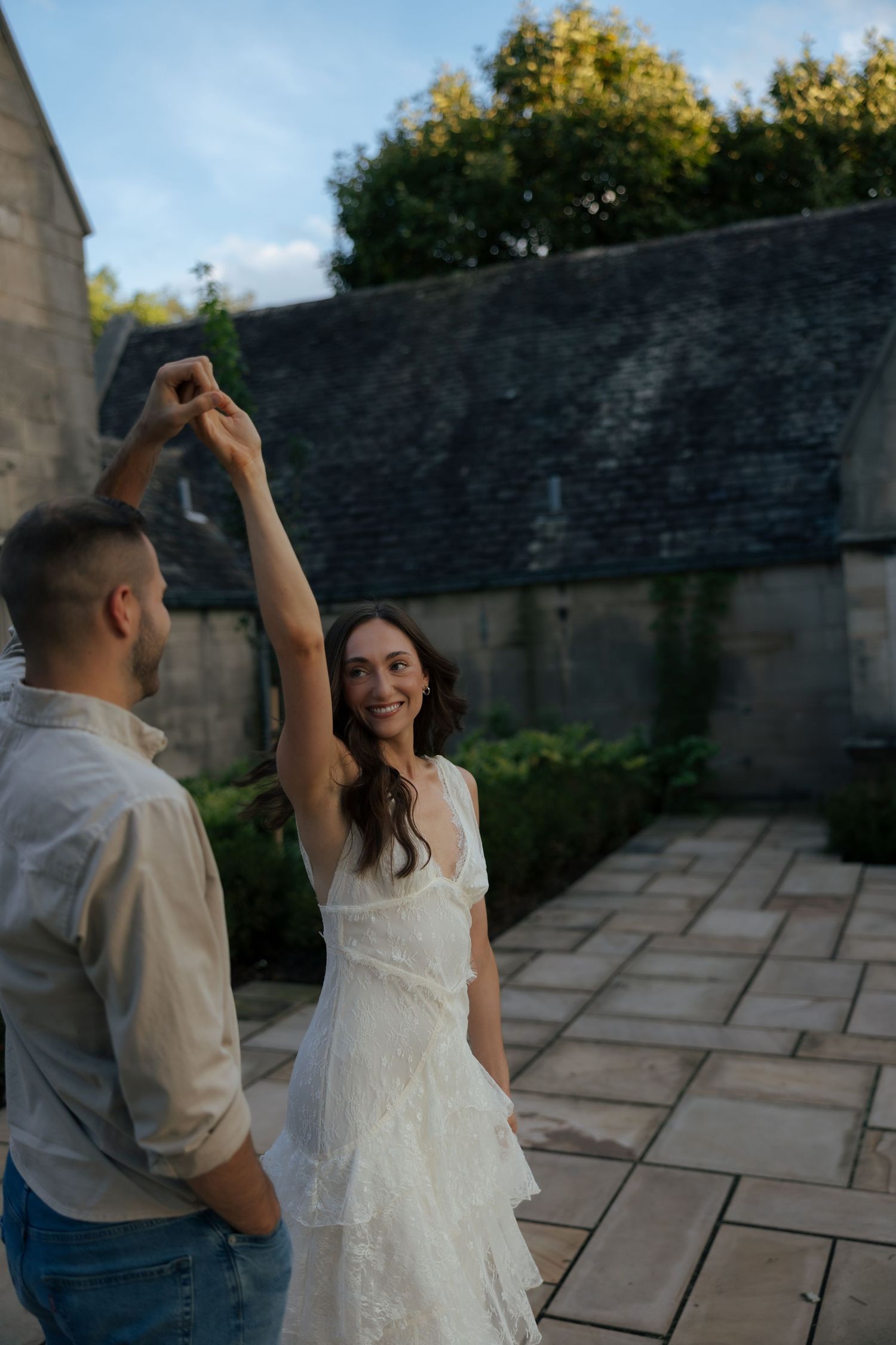 Bride in white dress dancing with groom outdoors at stone venue during golden hour.