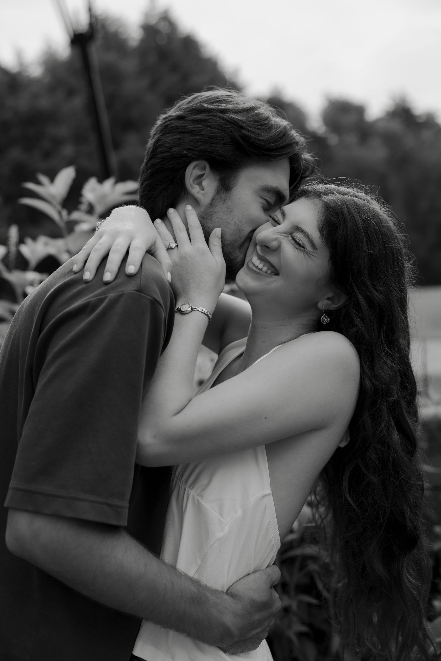 Black and white photo of joyful couple embracing and laughing together outdoors during engagement shoot.
