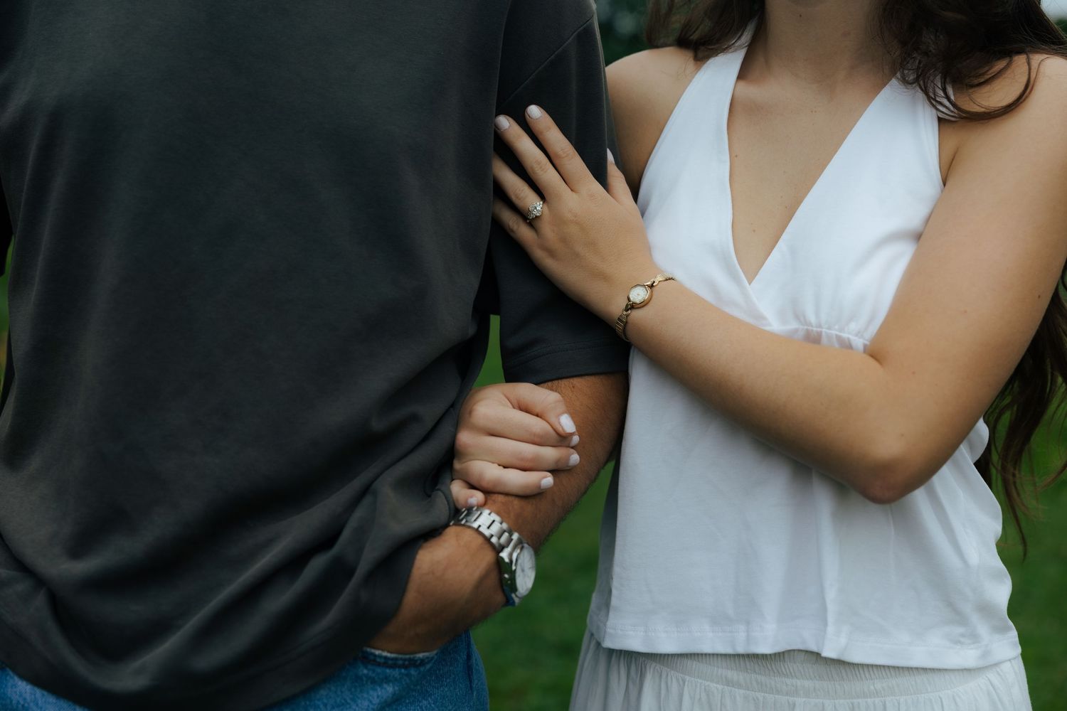 Couple holding hands outdoors, woman in white dress wearing a diamond ring and bracelet, man in black shirt.