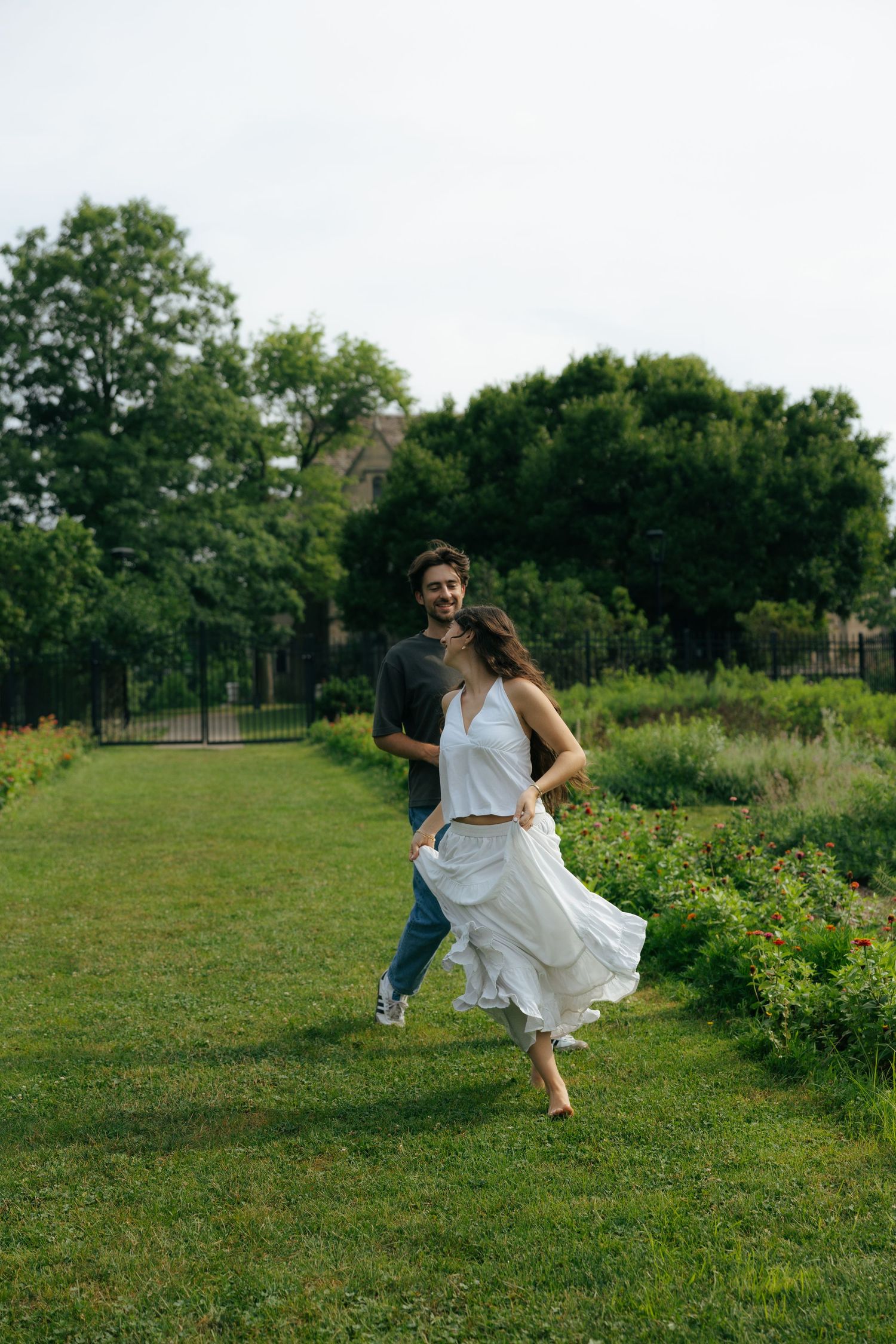 Happy couple walking together through a green park, woman in flowing white dress.