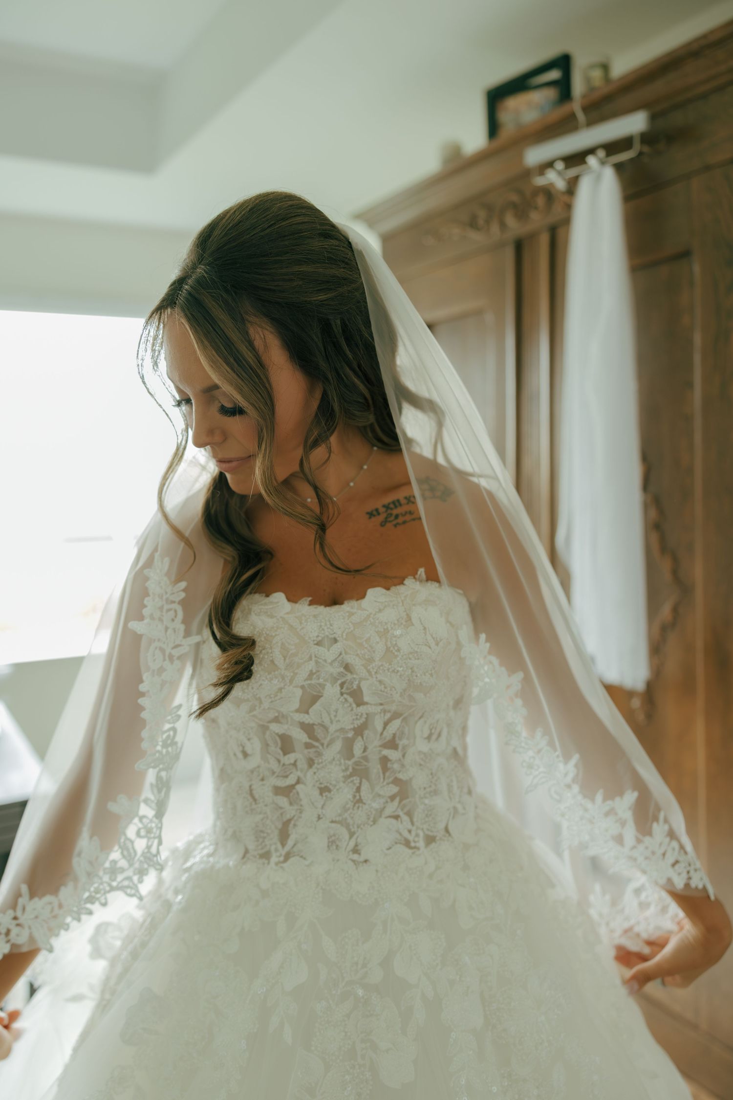 Bride in a lace ballgown wedding dress with a cathedral veil looking down in soft natural light.