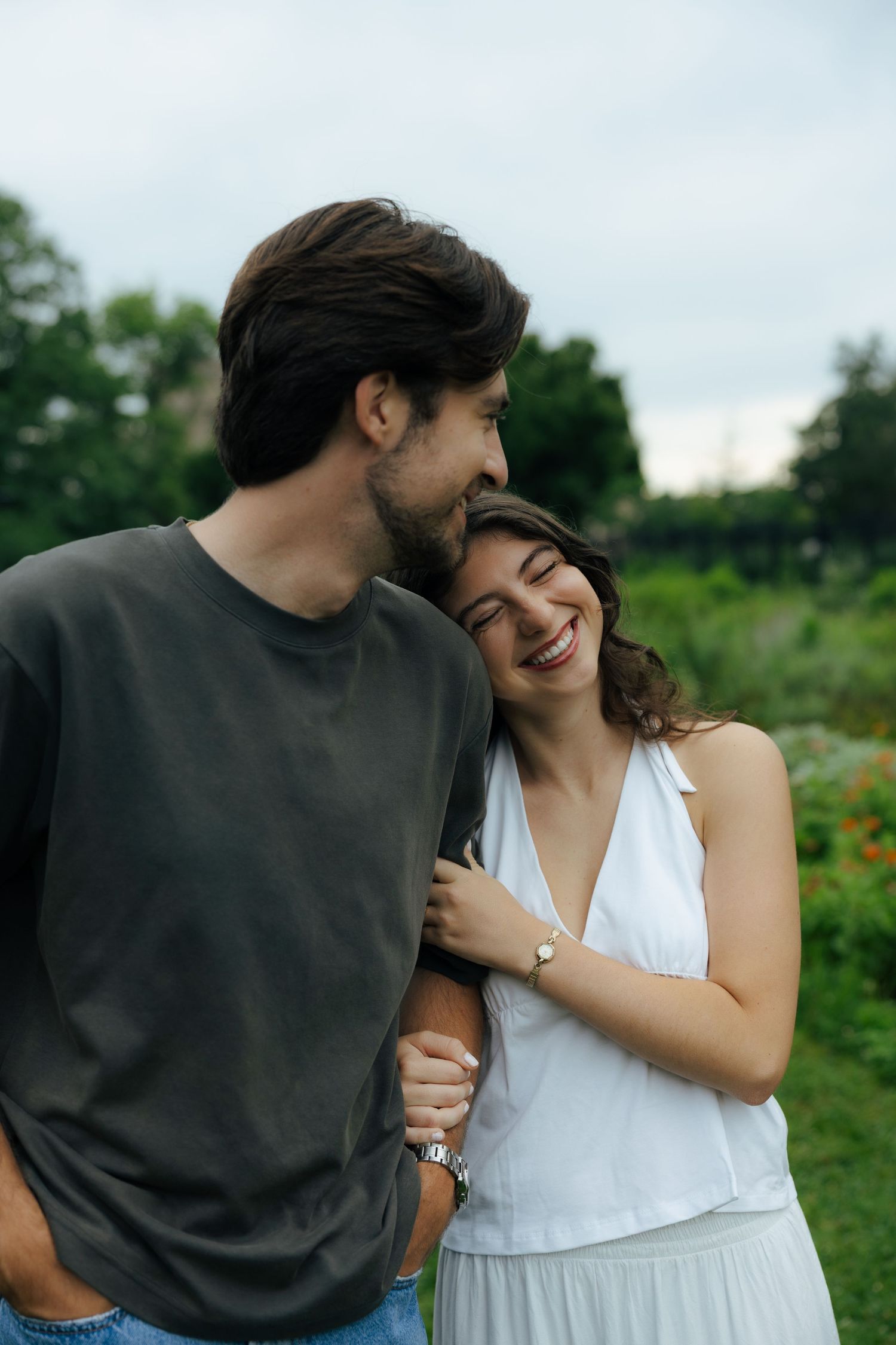 Joyful woman laughs while leaning on her partners shoulder outdoors in a lush green garden setting.