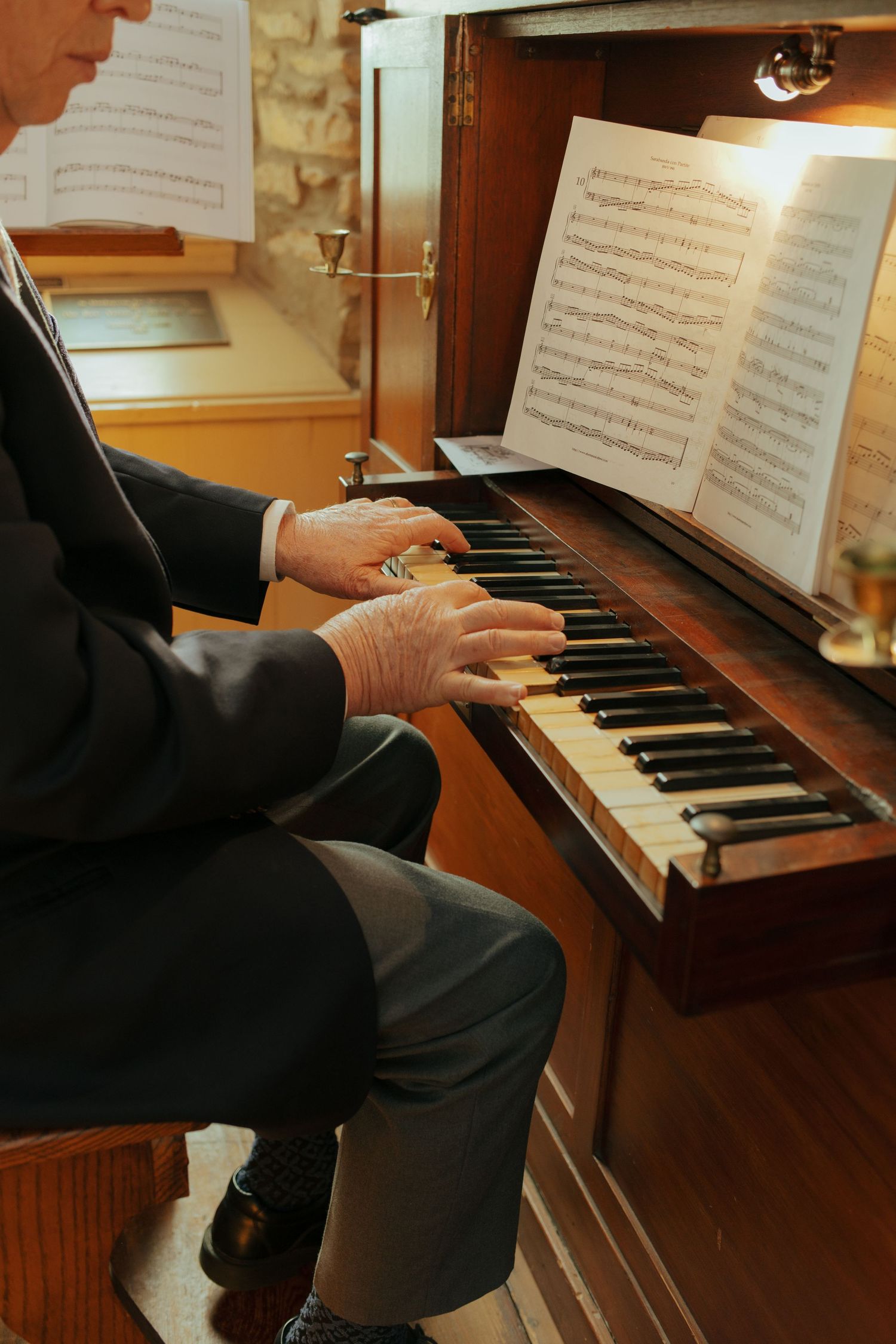 Close-up of elderly mans hands playing wooden pipe organ keys with sheet music on stand.