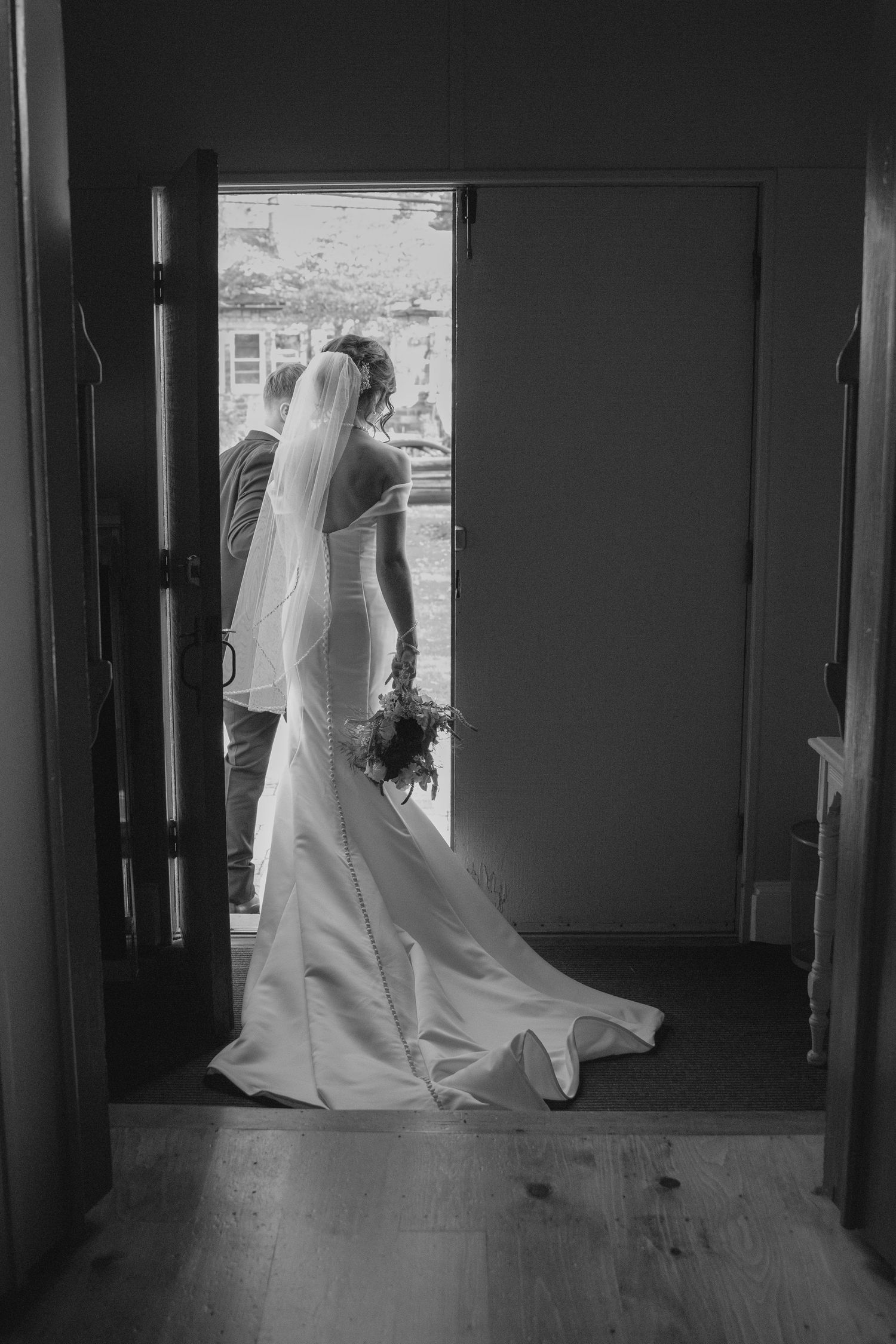 Black and white photo of bride in elegant gown exiting church doorway after ceremony.