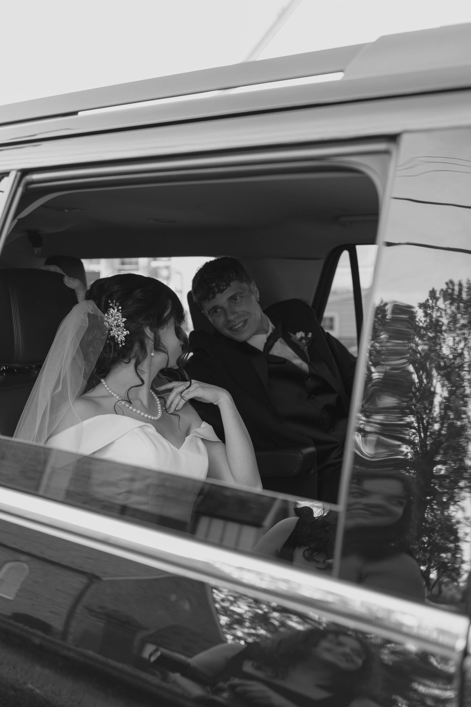 Black and white photo of smiling bride and groom sitting together inside a vehicle after their wedding.