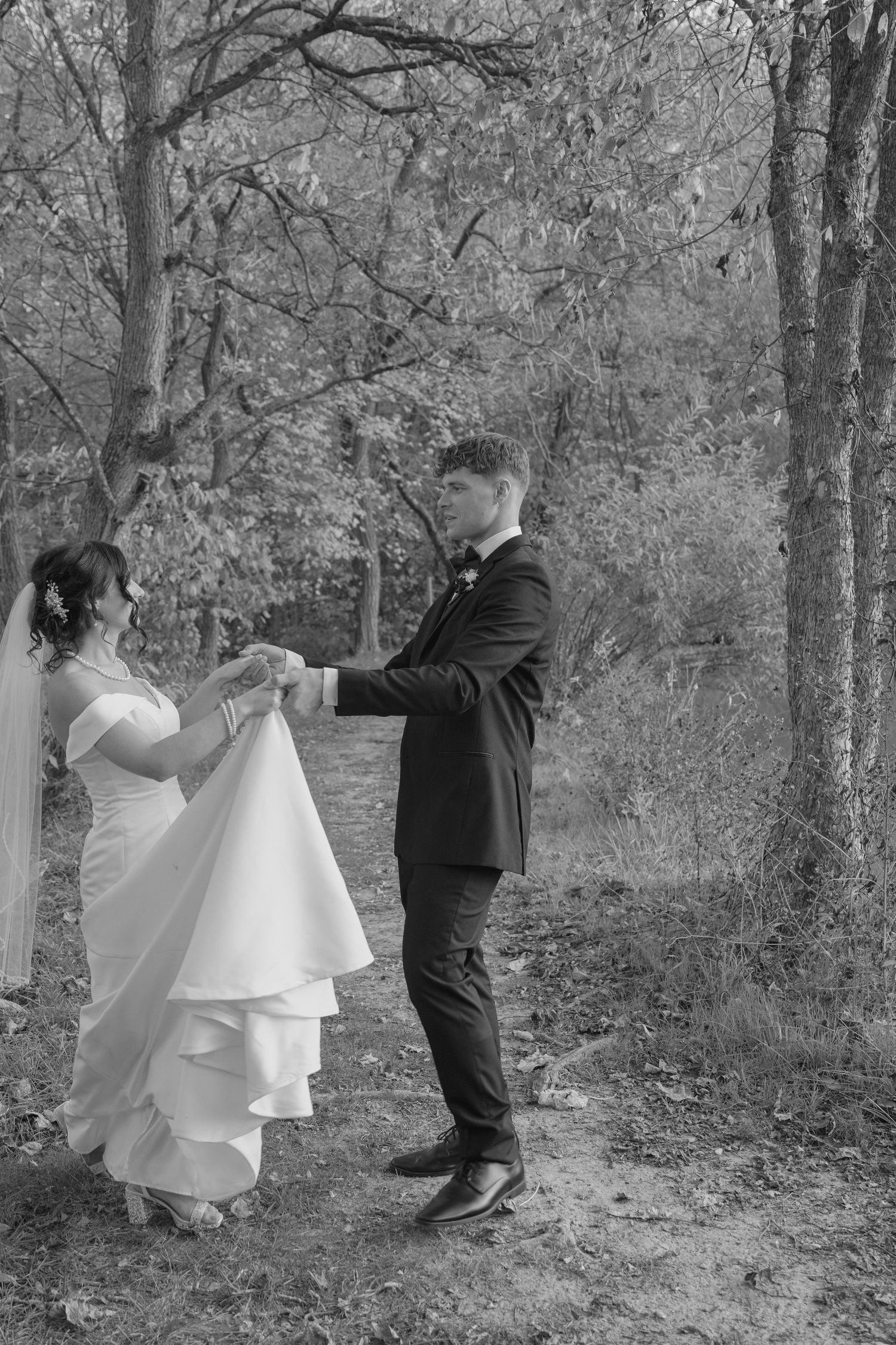 Black and white photo of bride and groom holding hands dancing in autumn forest wedding portrait.