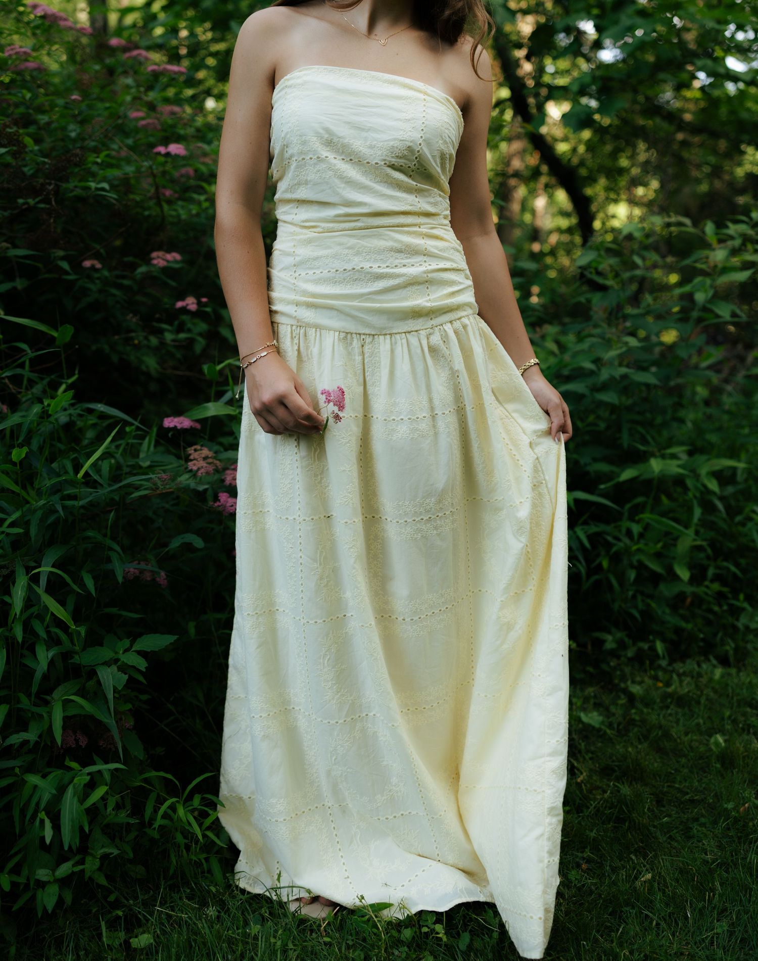Close-up of strapless cream eyelet maxi dress with pink flowers in garden setting.