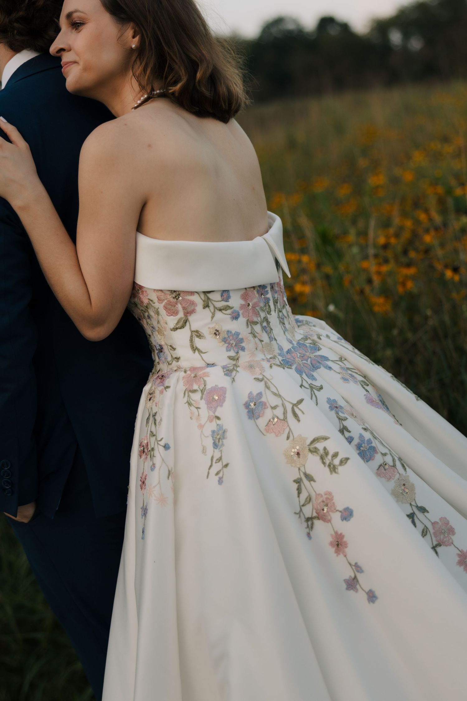 Close-up back view of bride in floral embroidered off-shoulder wedding gown in a sunflower field.