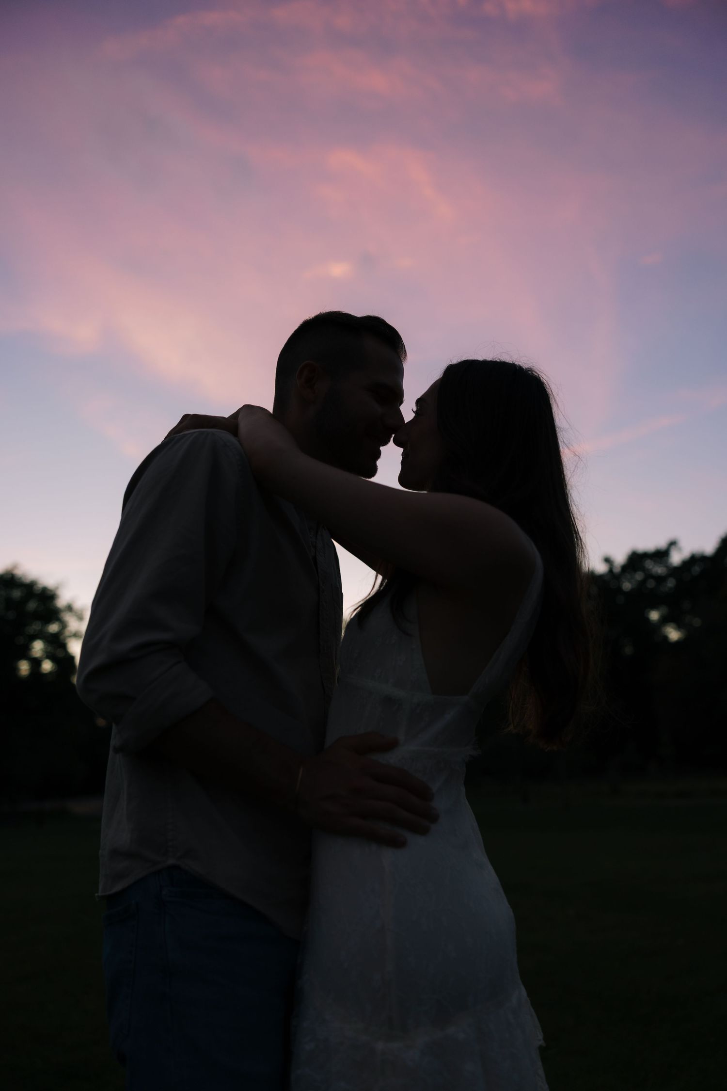 Romantic couple silhouette sharing an intimate moment against a stunning pink and purple sunset sky.