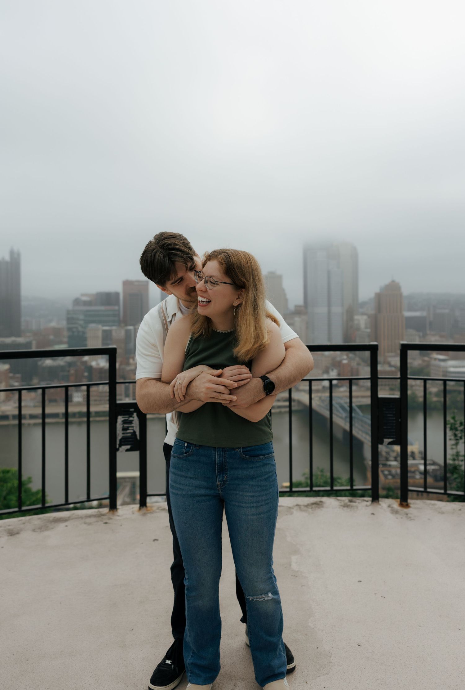 Happy couple embracing on a rooftop overlook with a misty city skyline in the background.