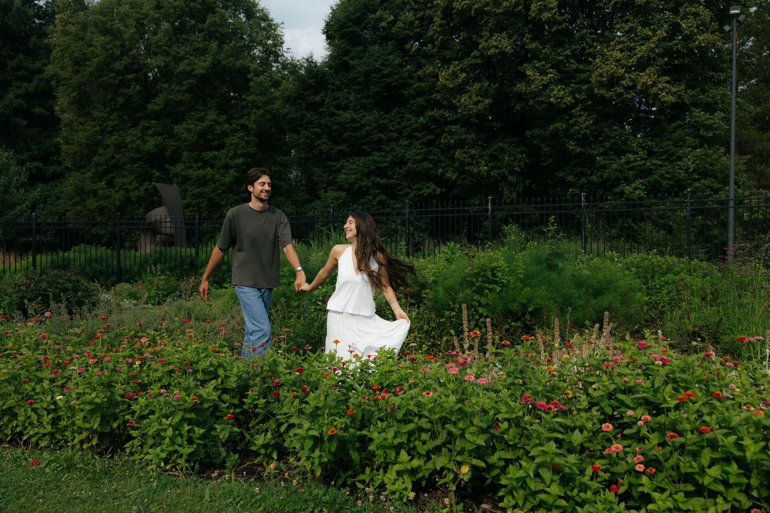 Happy couple holding hands while walking through a vibrant garden with colorful flowers.