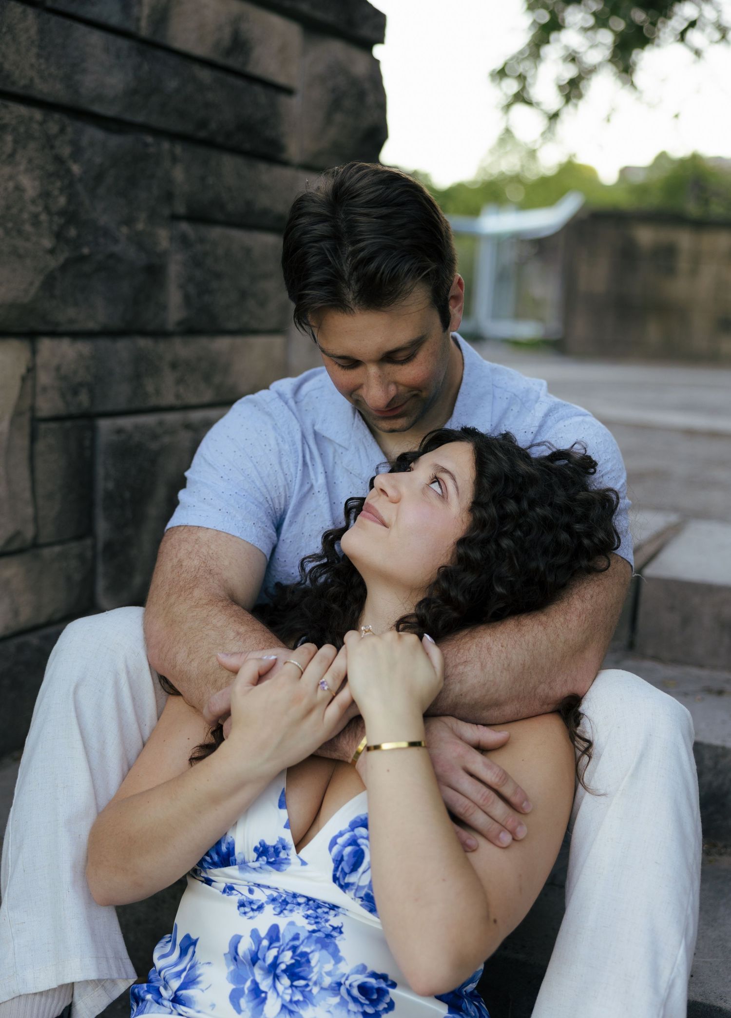 Man embracing woman from behind on steps as she gazes up at him lovingly.