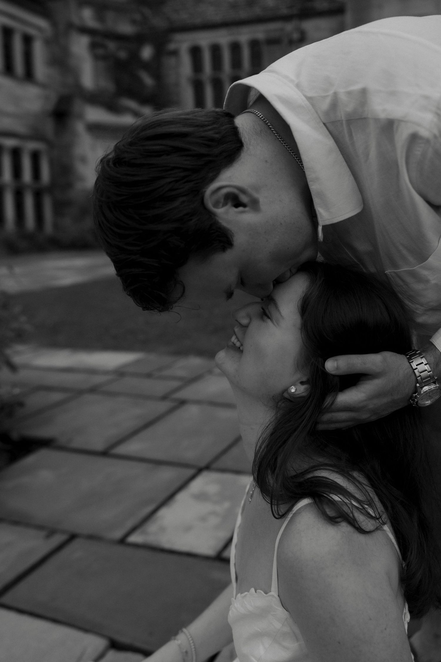 Black and white photo of a couple sharing a romantic kiss outdoors on a stone patio.