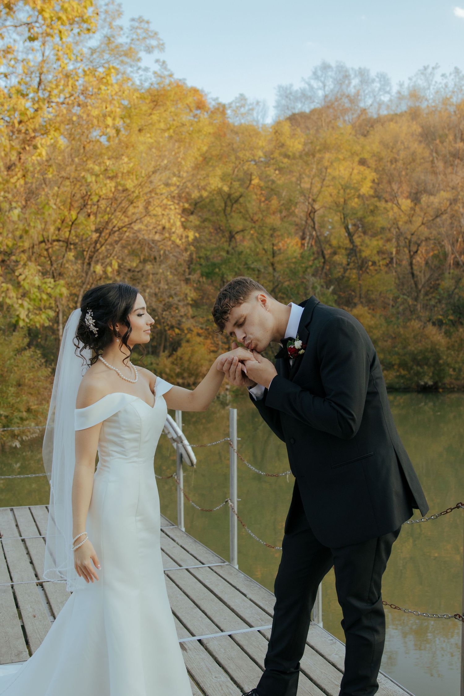 A romantic moment between newlyweds on a wooden dock surrounded by autumn foliage.